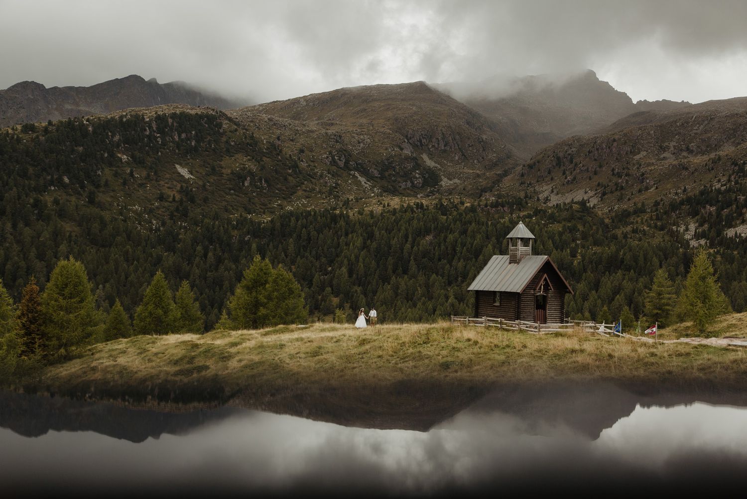 Scenic mountain landscape with fog rolling over peaks and a tranquil lake reflecting the cloudy sky and forest.
