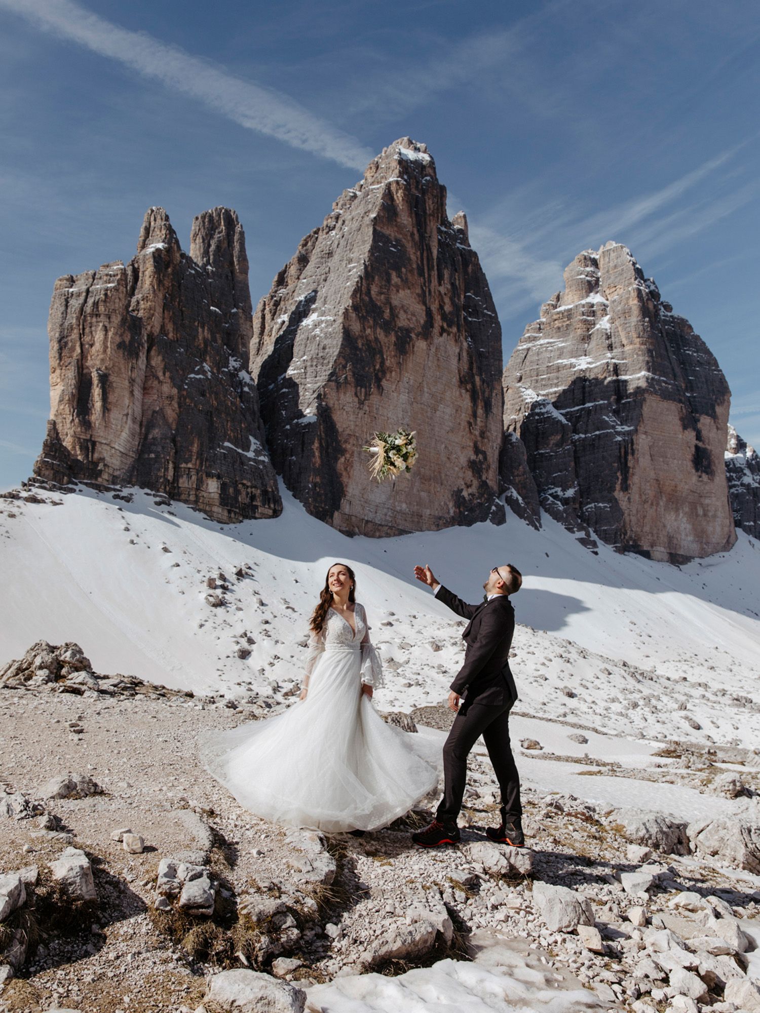 A couple in wedding attire poses in front of dramatic snow-covered mountain peaks in the Dolomites.