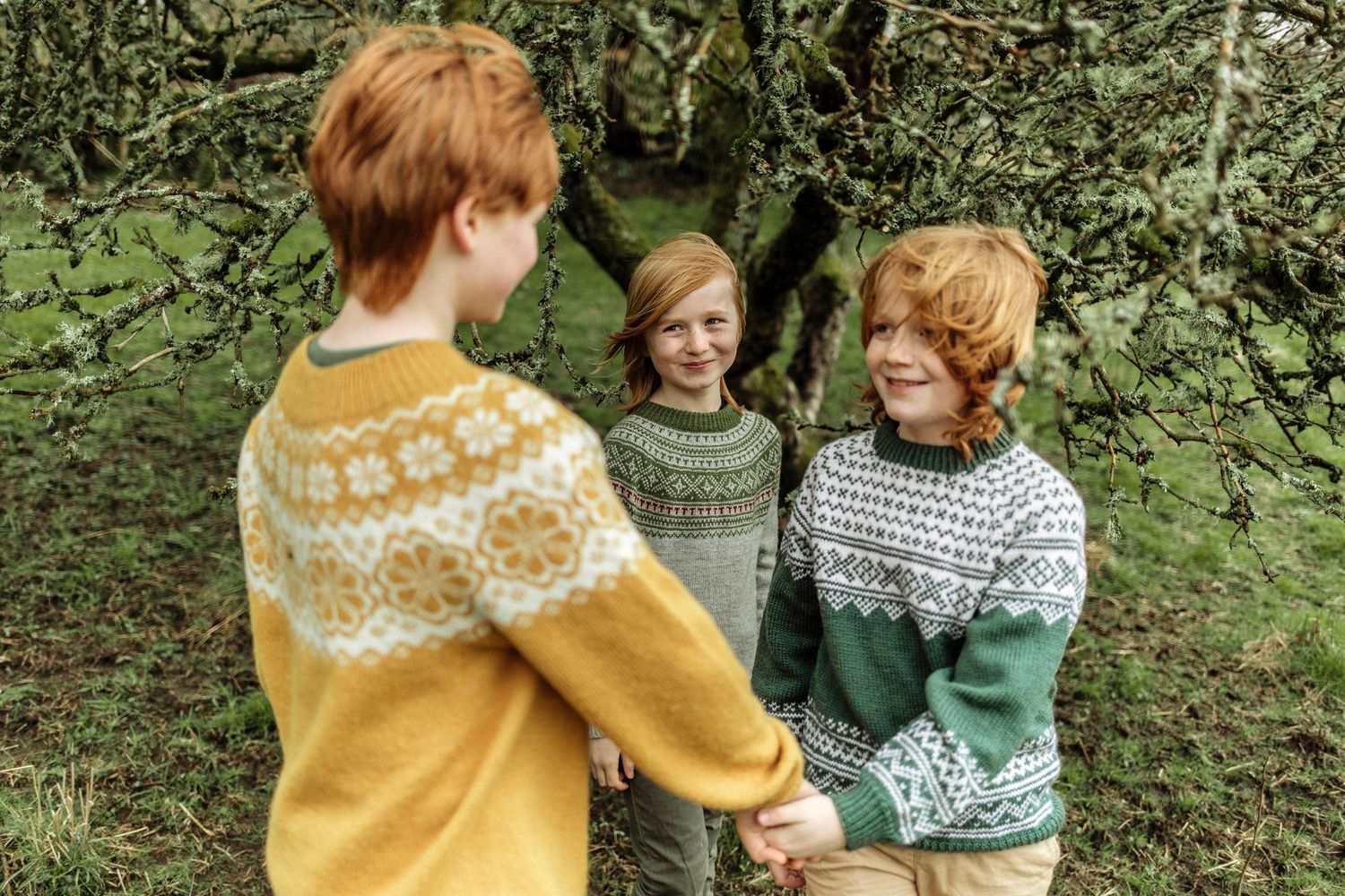 Children wearing colorful knit sweaters playing together outdoors.