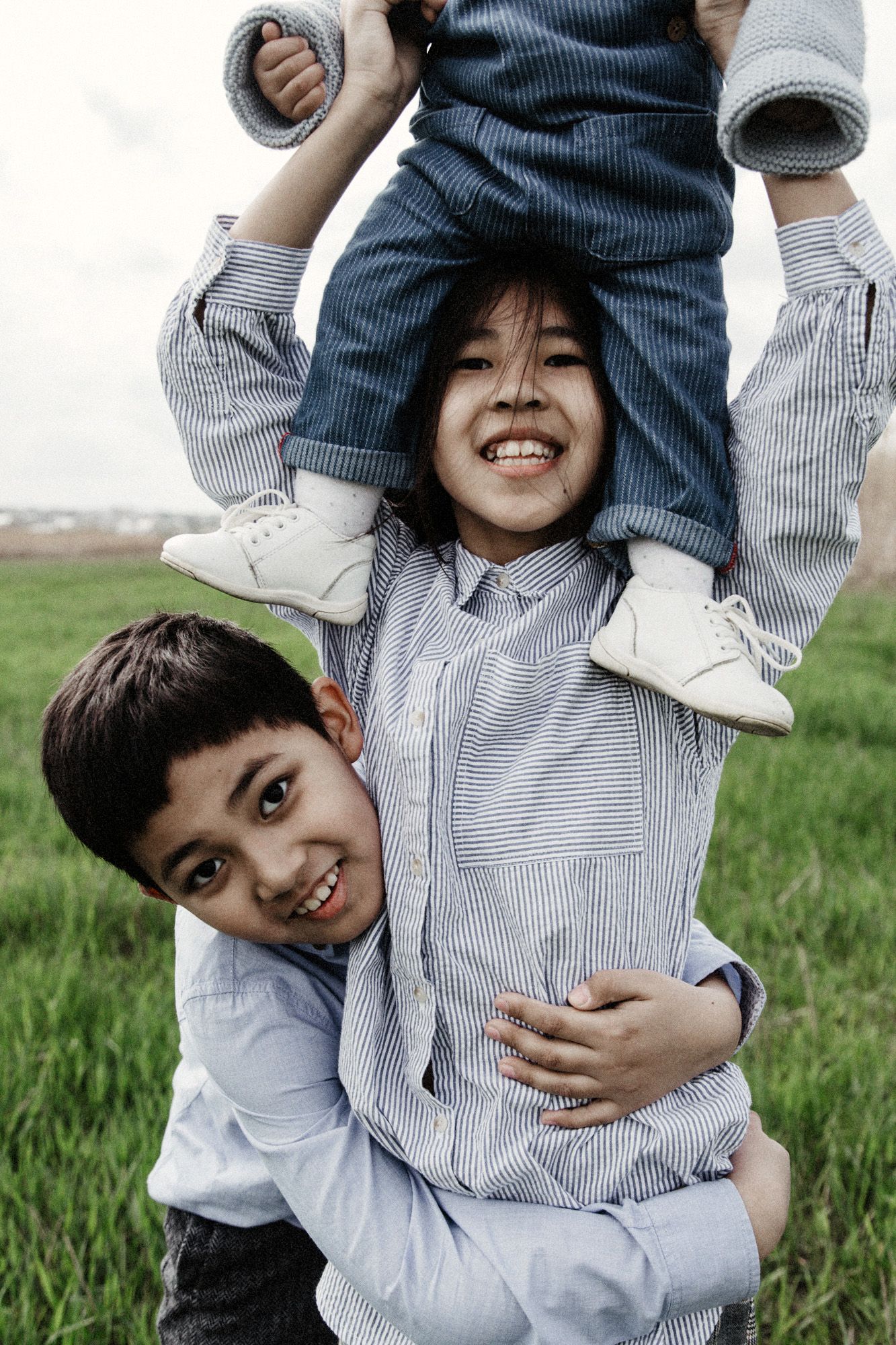 Playful moments captured in a grassy field as children are lifted up and held in joyful poses.
