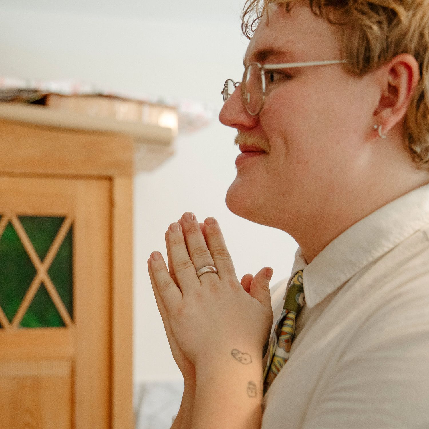 Person wearing glasses and white shirt clasps hands together with joyful expression.