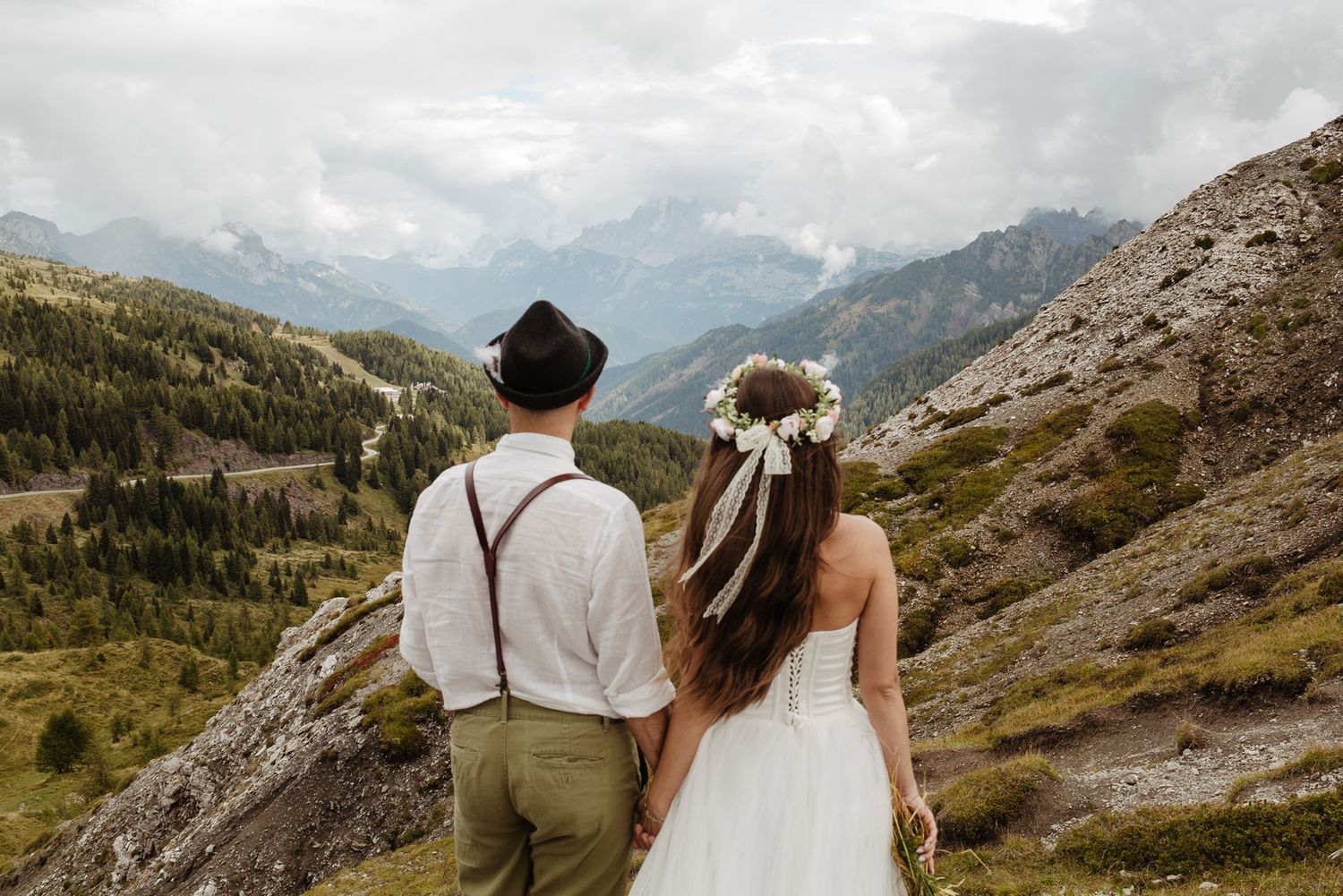 A couple in wedding attire admires mountain views from a scenic overlook in the Alps.