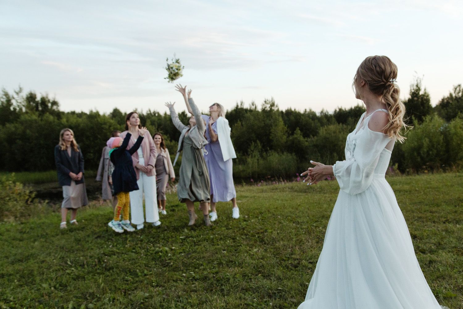 Wedding party scattered across a green field during sunset.