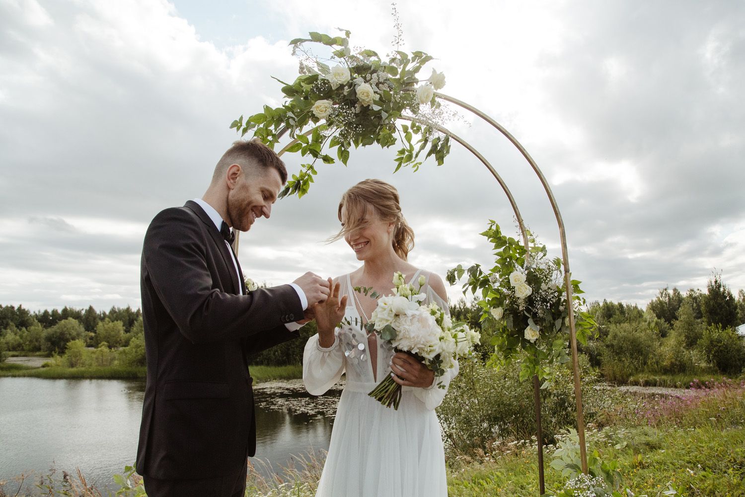 Wedding celebration with floral arch and natural lake scenery in background.
