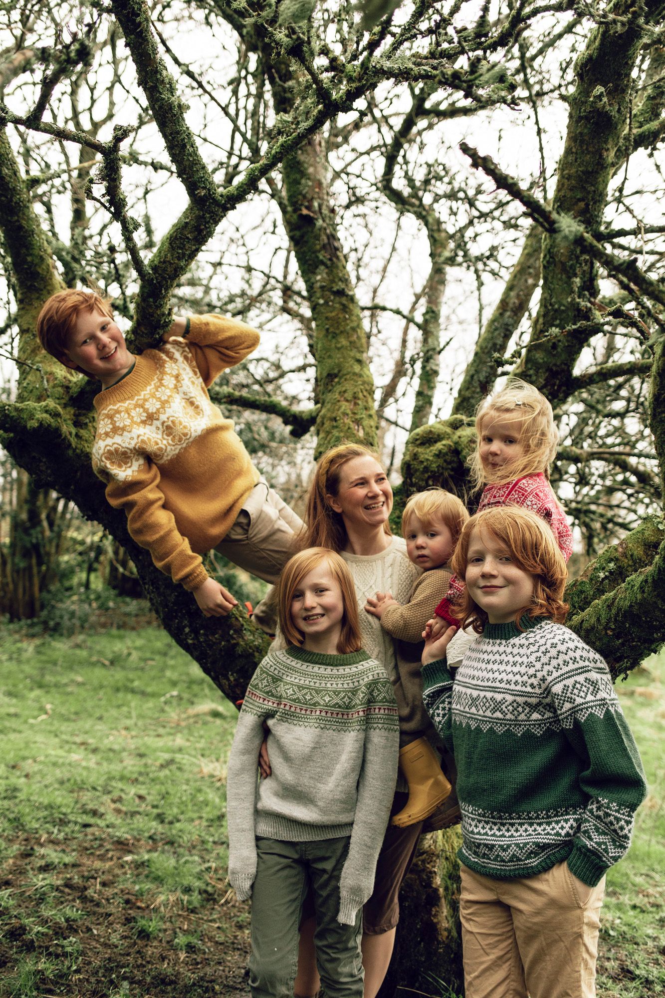 A group wearing cozy knit sweaters plays and laughs together among trees in an outdoor setting.