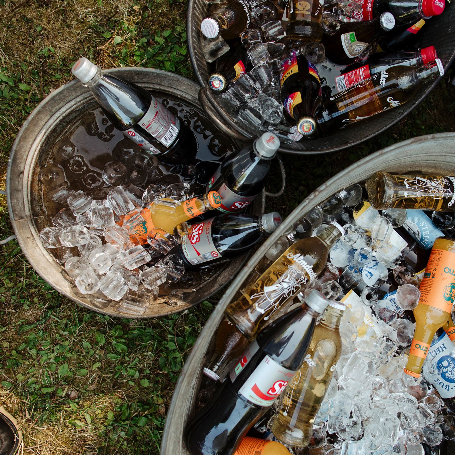 Assorted bottles of beverages chilling in ice buckets at an outdoor gathering or party setting.