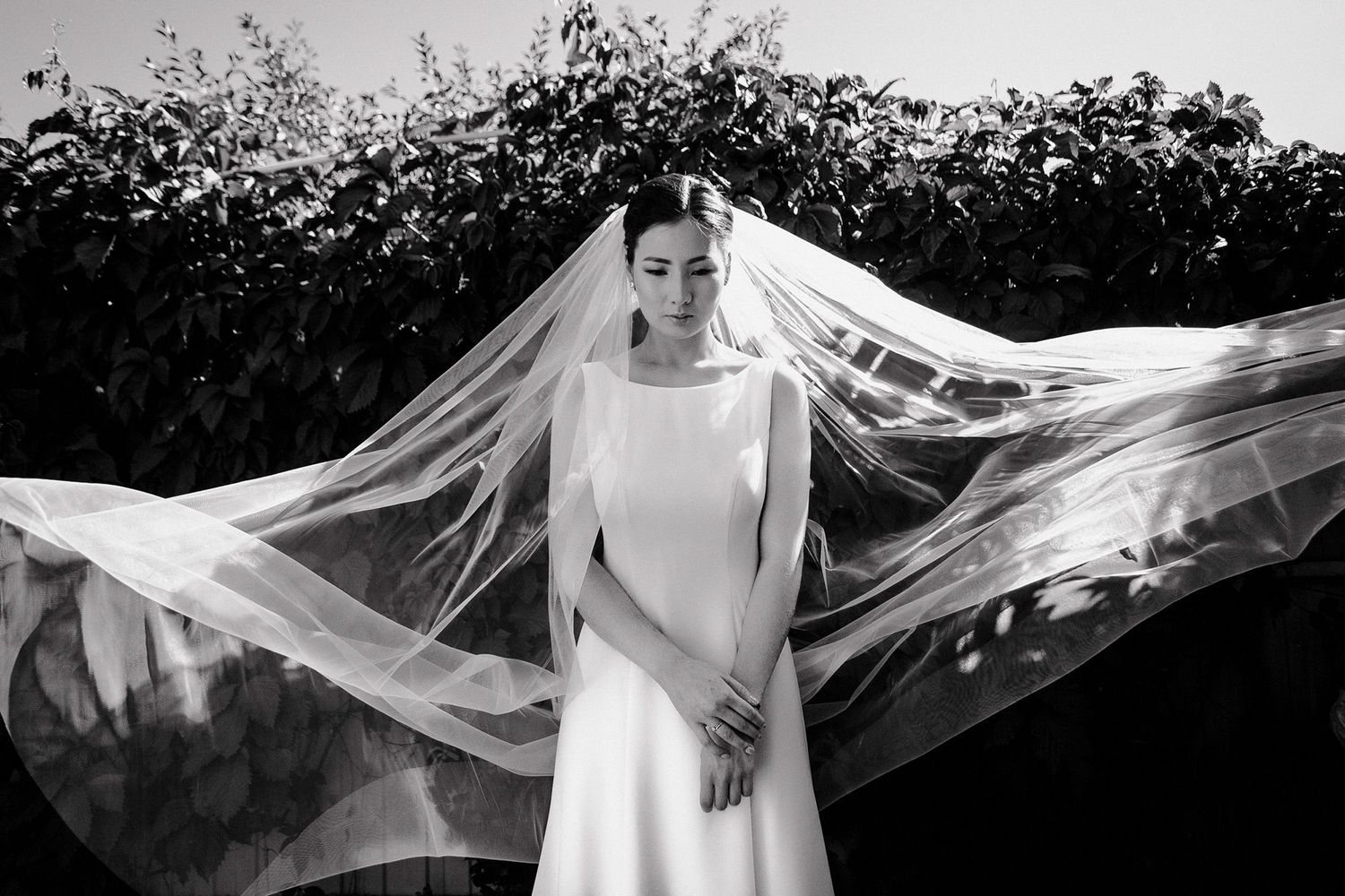 A flowing wedding veil catches the breeze in an artistic black and white bridal portrait series.
