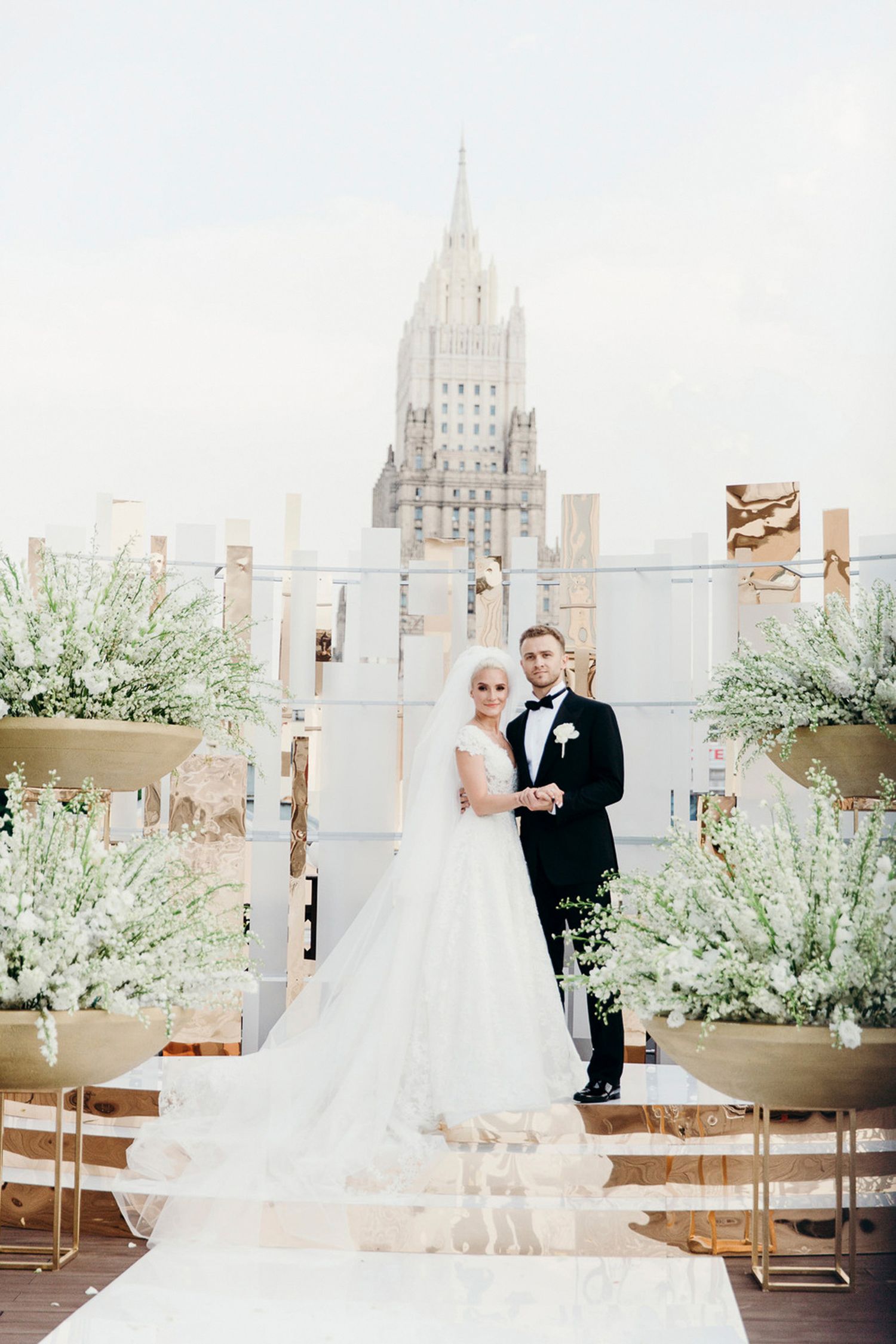 Elegant wedding couple poses in a bright white venue with modern decor and greenery accents.