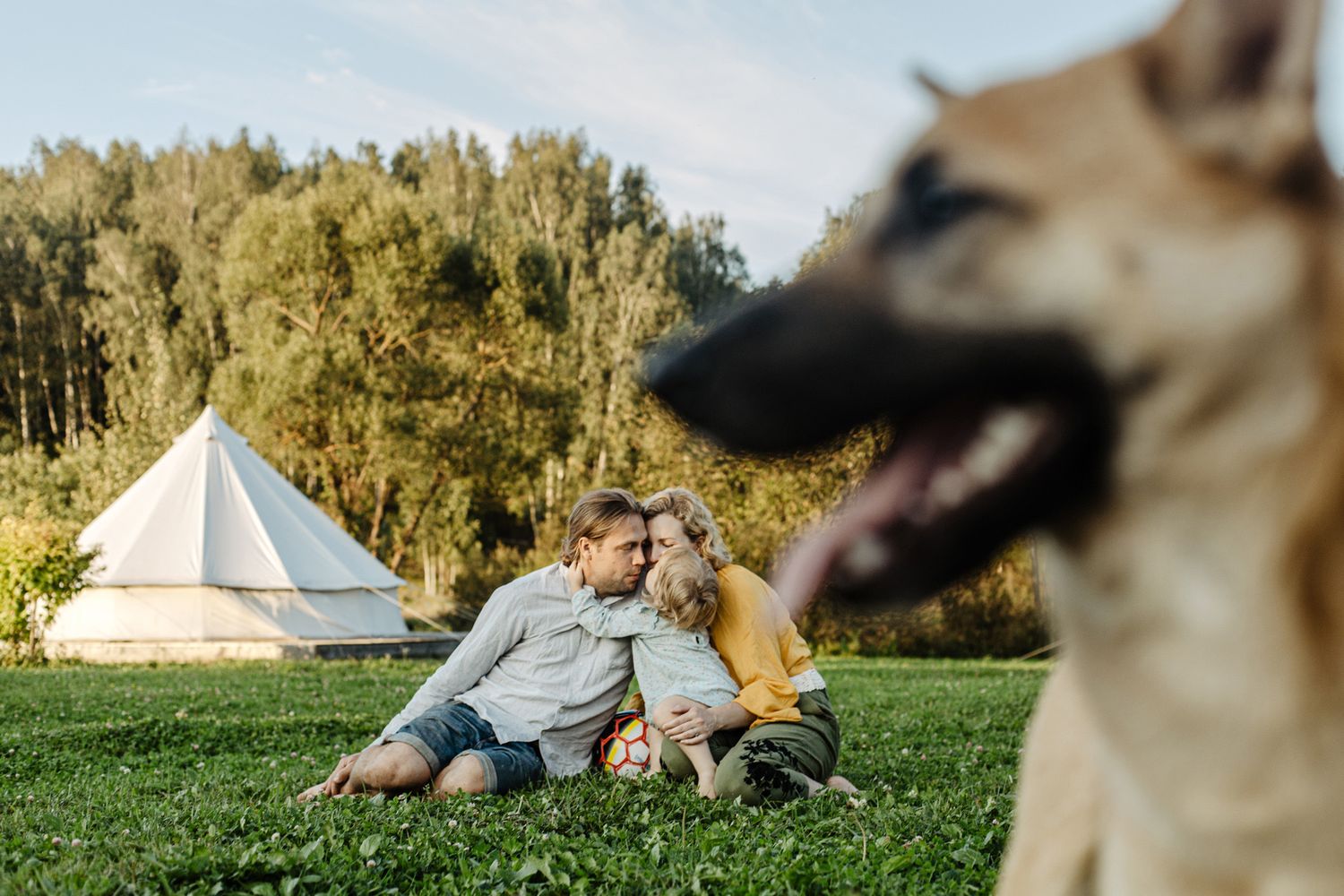 Couple relaxing on grass field with teepee tents in background during golden hour.