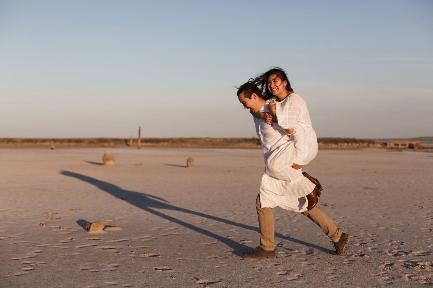 A couple embraces on a sandy beach during sunset creating silhouettes against the warm sky.