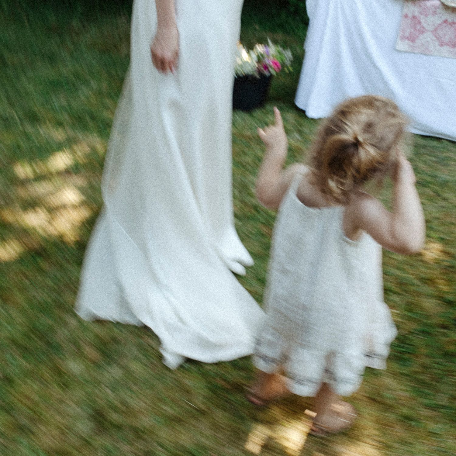 Motion-blurred image of people in white dresses walking on grass during an outdoor event.