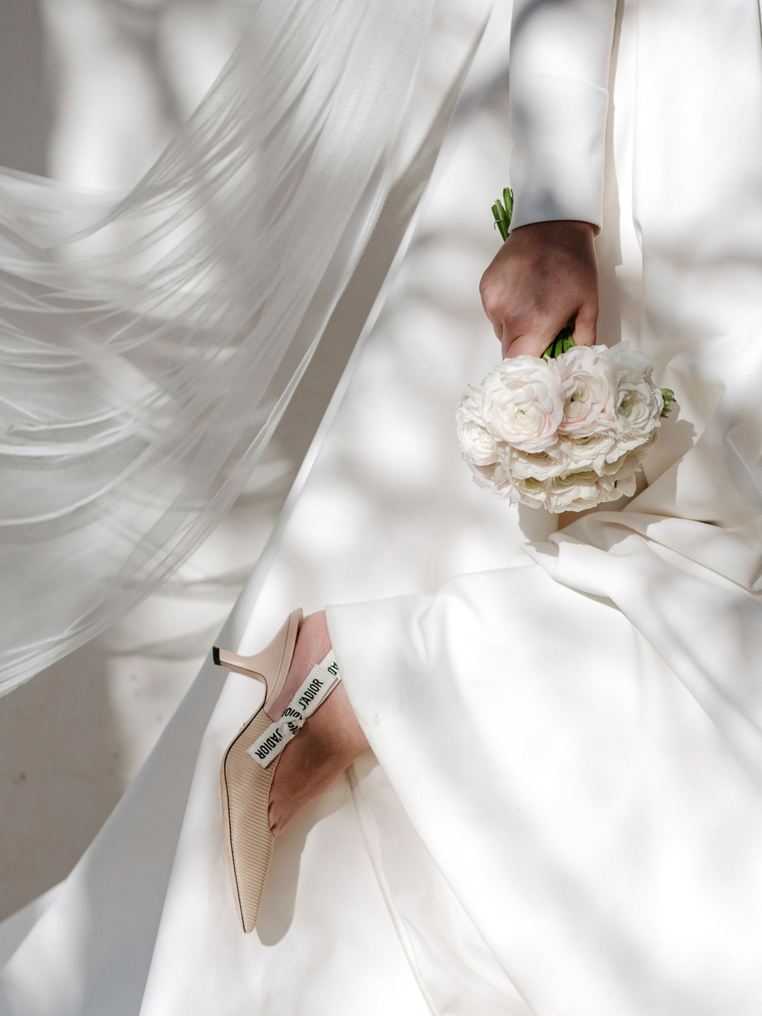 Elegant white bridal shoes and delicate floral bouquet arranged in a minimalist composition with soft natural lighting.