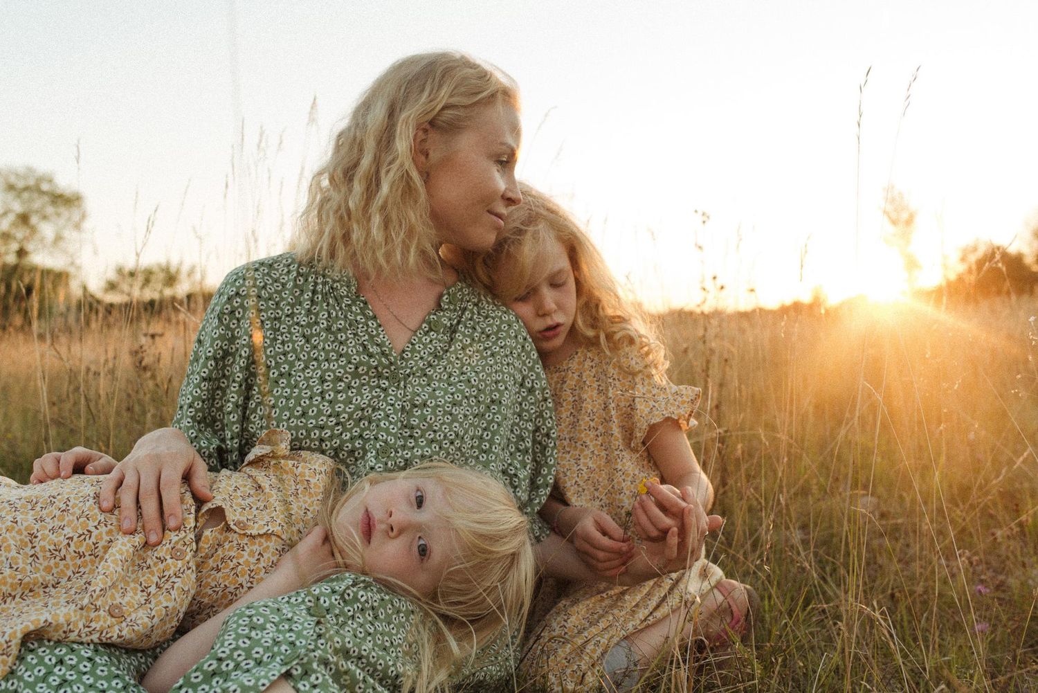 Mother and daughter lying in golden grass field during sunset with warm glowing light in background.