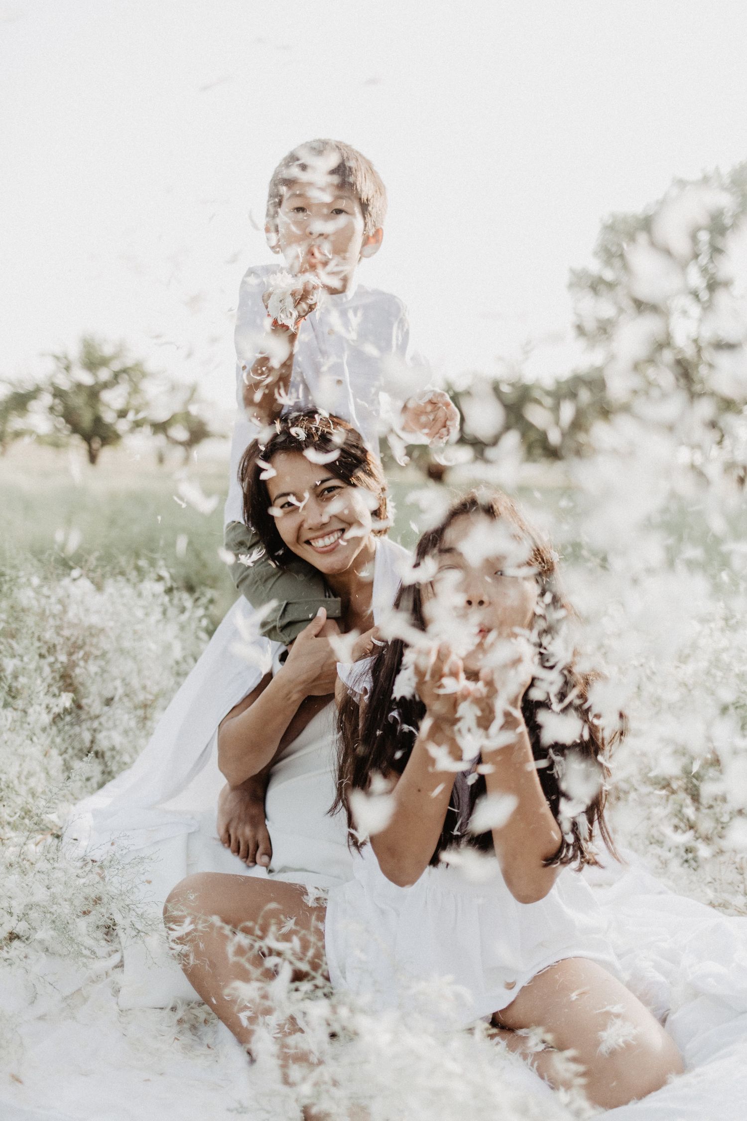 Two people playfully throw white feathers in the air during a romantic outdoor photoshoot.