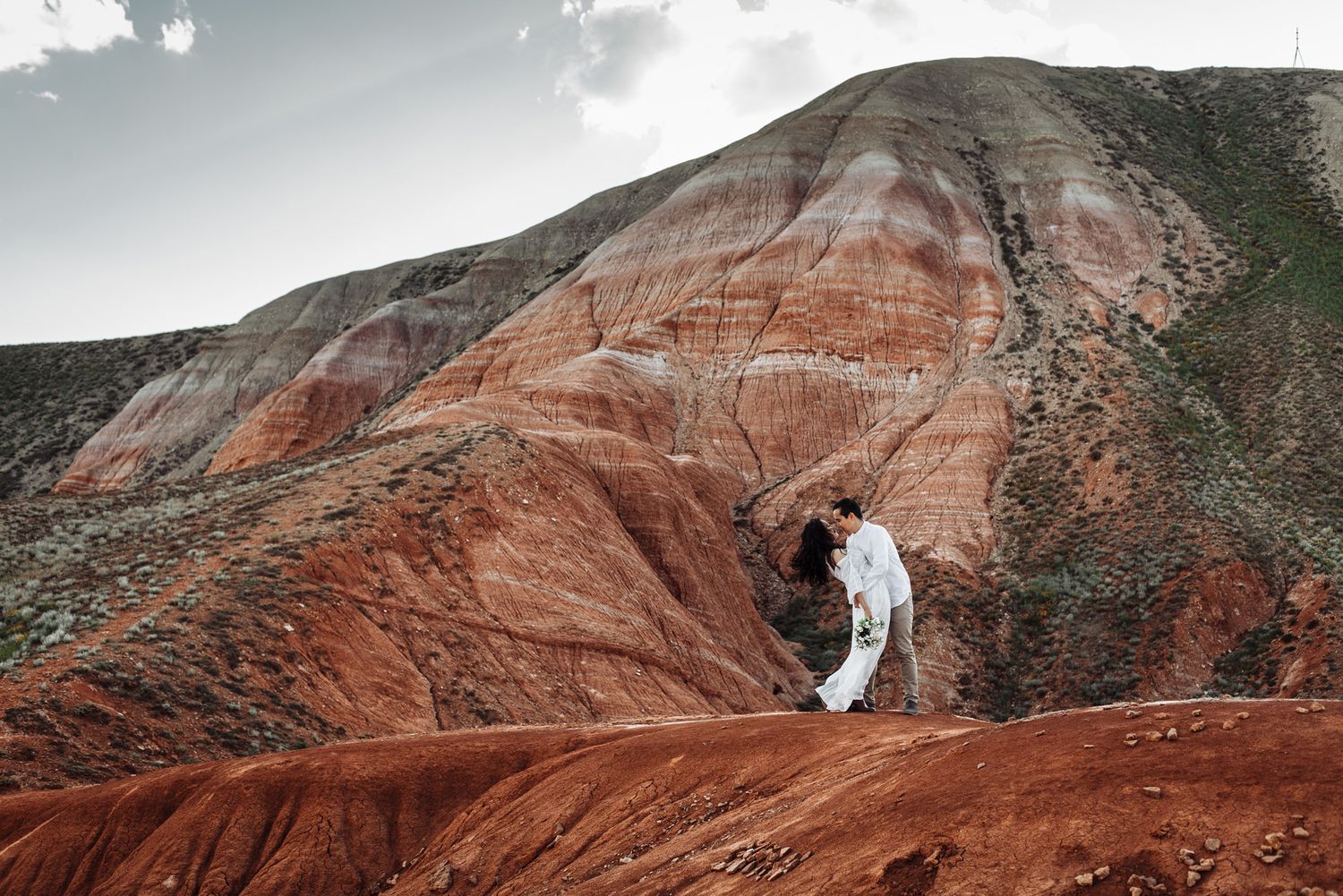 A panoramic view of red rock formations and cliffs in a mountainous desert landscape at sunset.