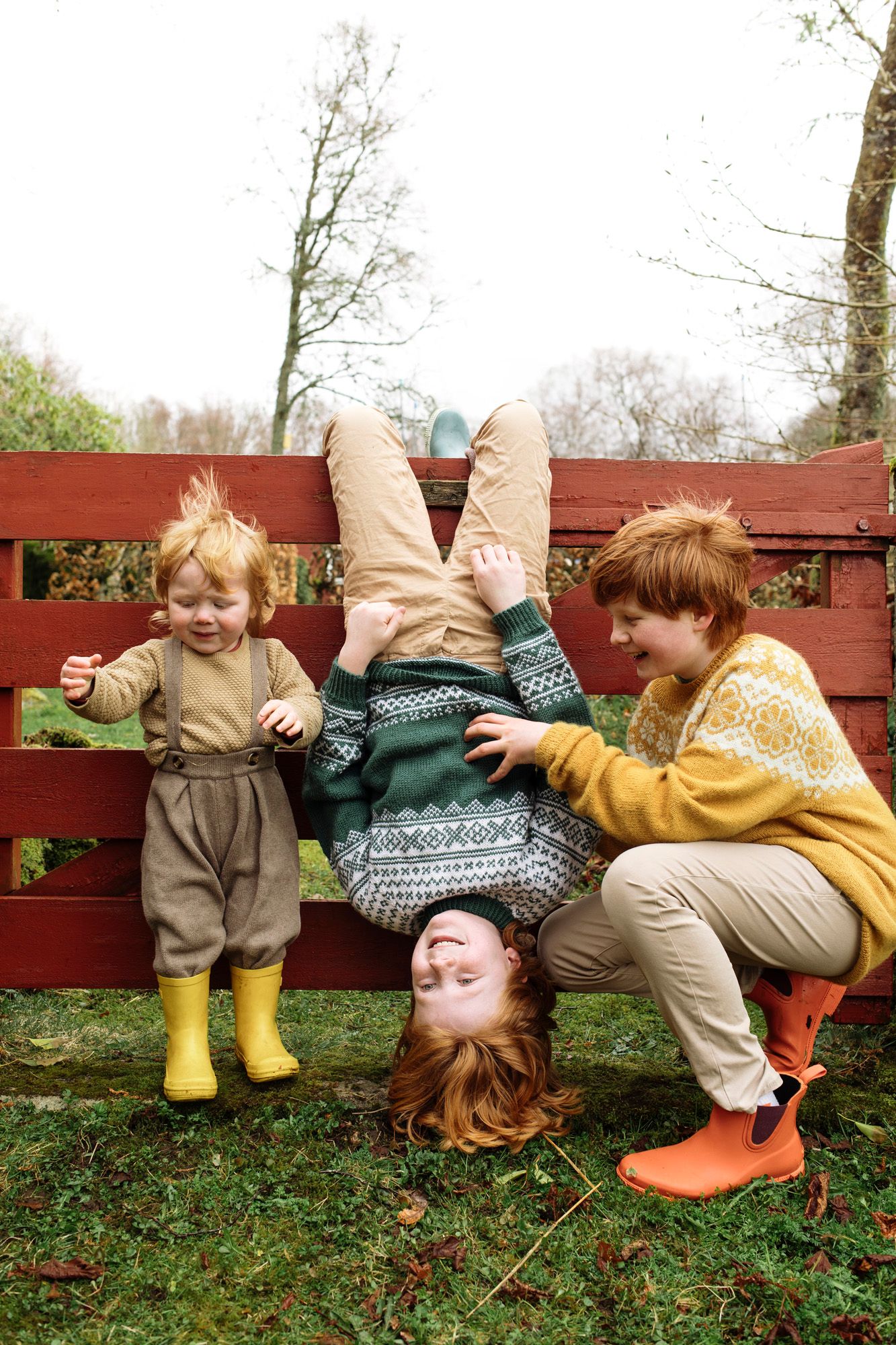 Playful scene with yellow boots and matching sweaters on red wooden fence.
