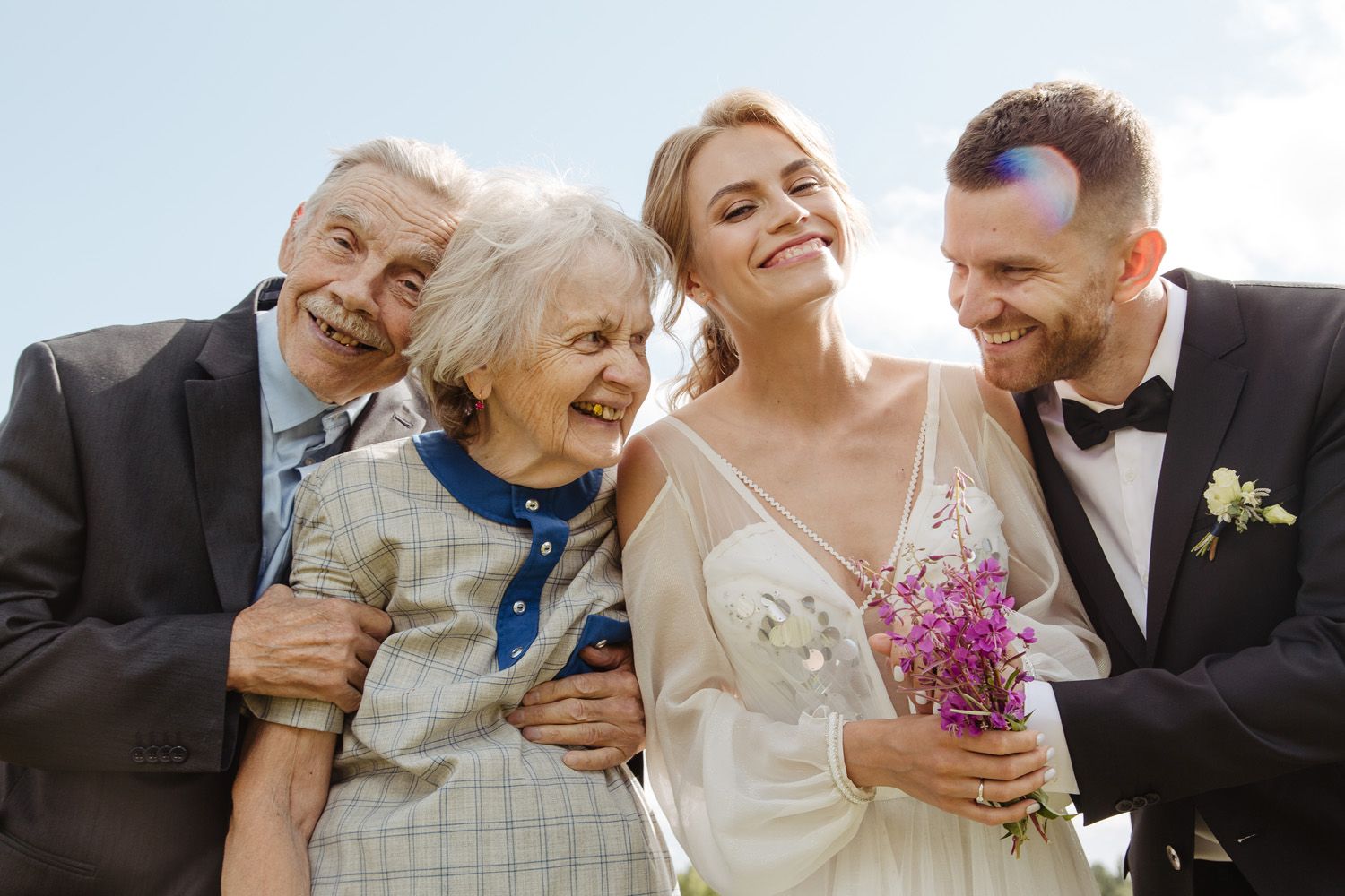Wedding party sharing joyful moment outdoors with bouquet of pink flowers.