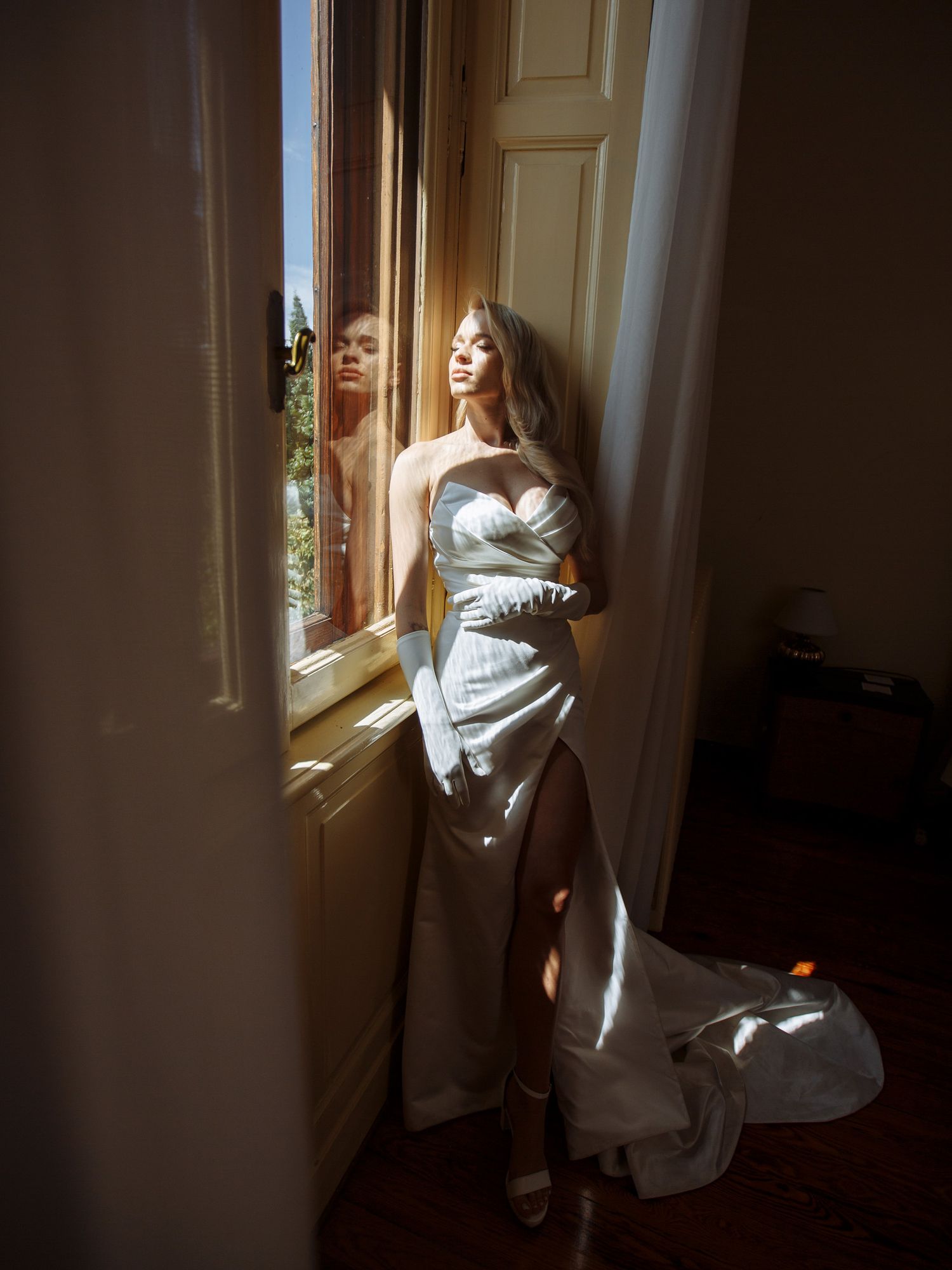 Artistic series of photos showing a figure wrapped in white fabric standing by a sunlit window in moody lighting.