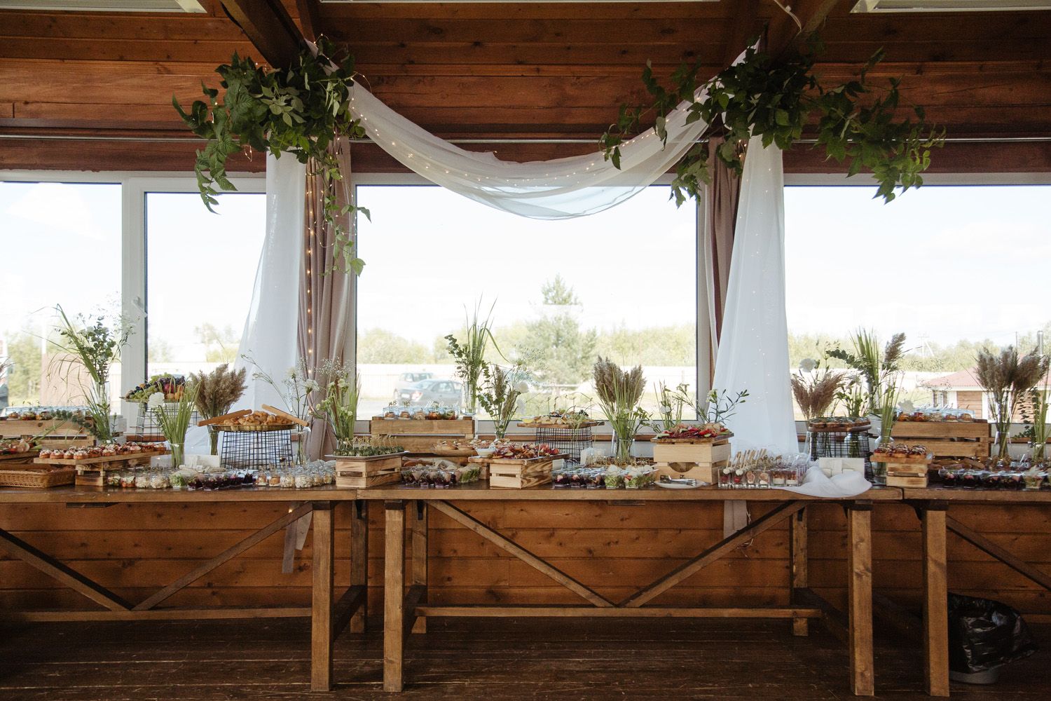 Rustic wedding reception table setup with white draping and greenery decorations.
