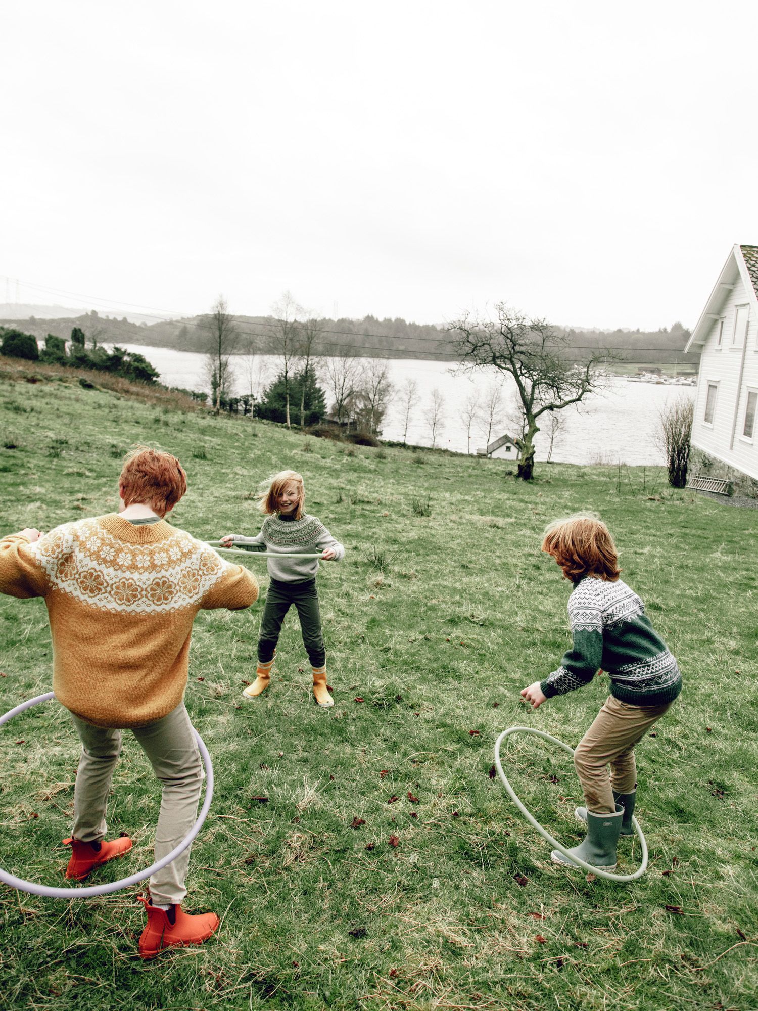 Four sequential photos show people playing with hula hoops on a grassy hillside overlooking a lake on an overcast day.