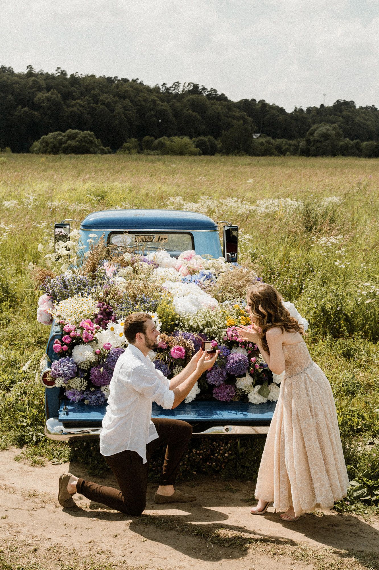 Vintage blue pickup truck filled with colorful flowers parked in a sunny meadow during a summer photo session.