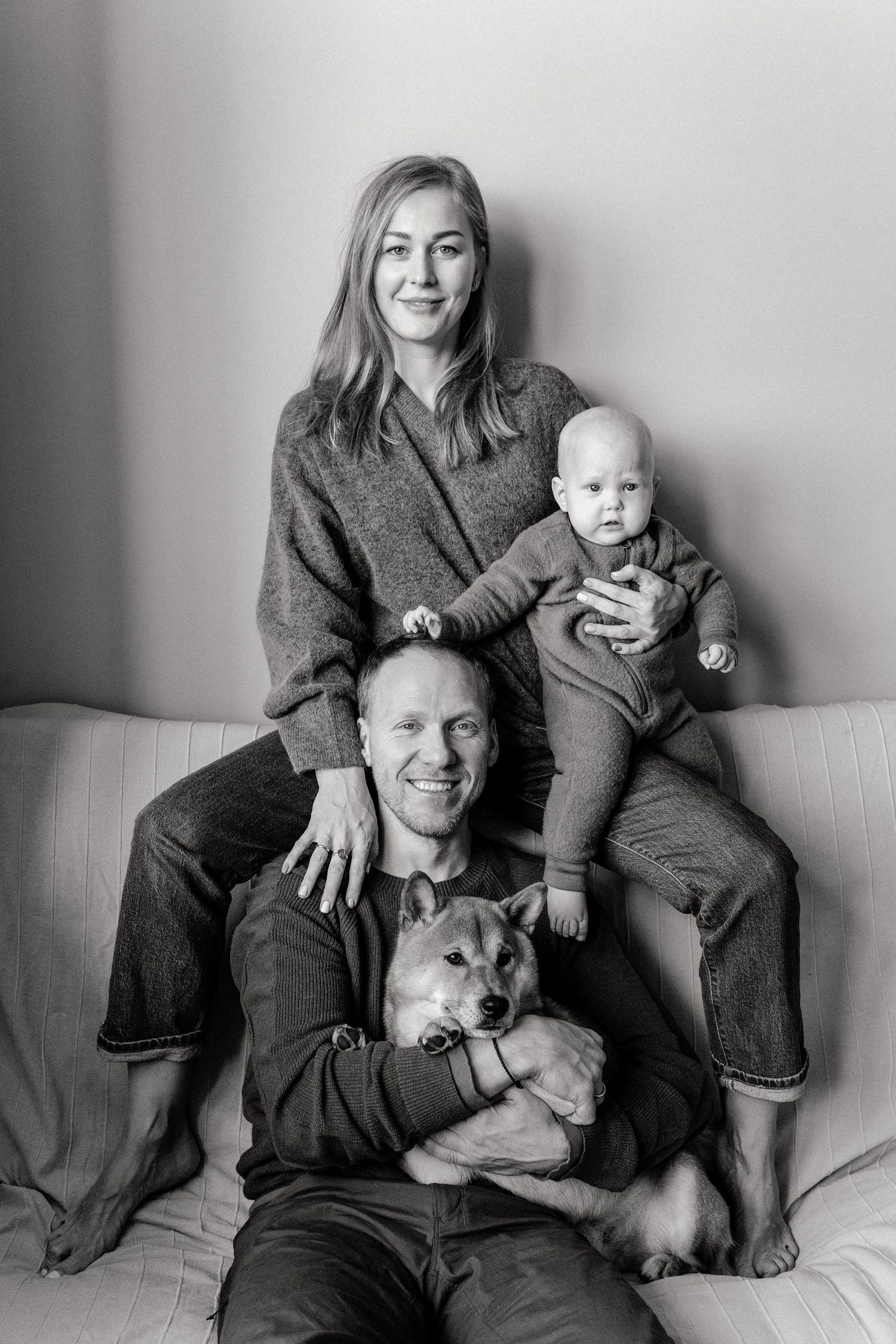 A black and white photo series showing a family posing together on a couch with their dog in casual attire.