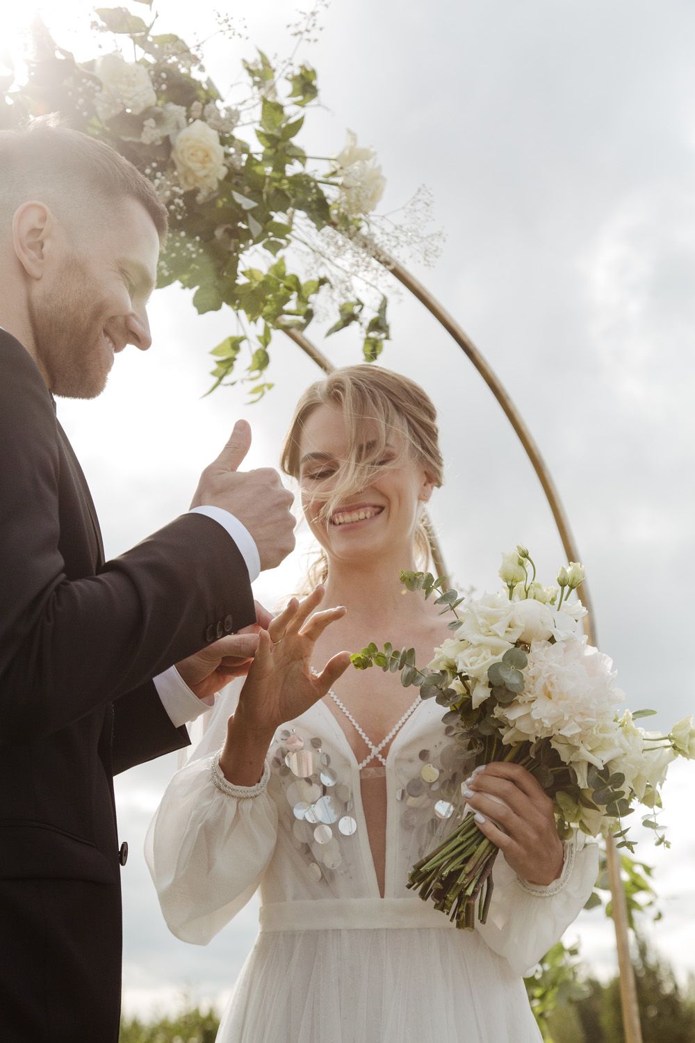 Joyful wedding moment under an elegant floral arch with white flowers.
