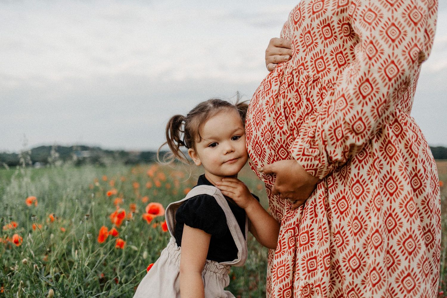 Family plays together in a vibrant field of orange poppies wearing a patterned dress.
