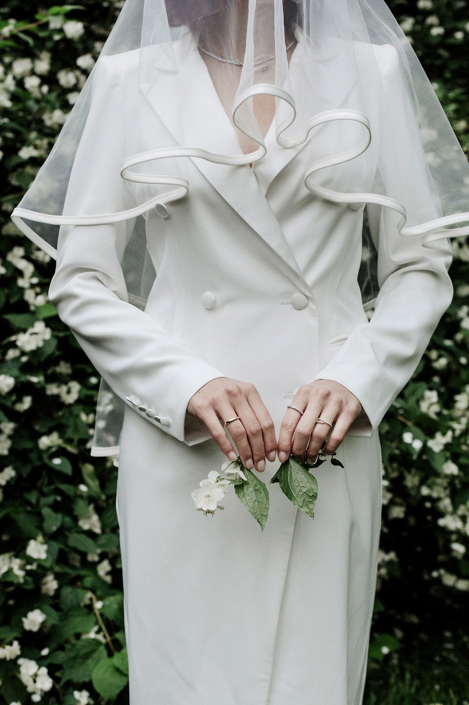 Close-up details of a white bridal outfit with ruffled collar and delicate white roses against a green garden background.