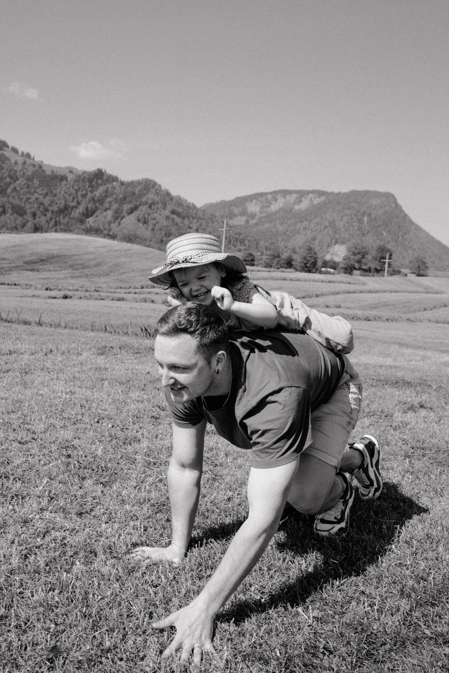 Black and white sequence of person crawling through grass field with mountains in background.