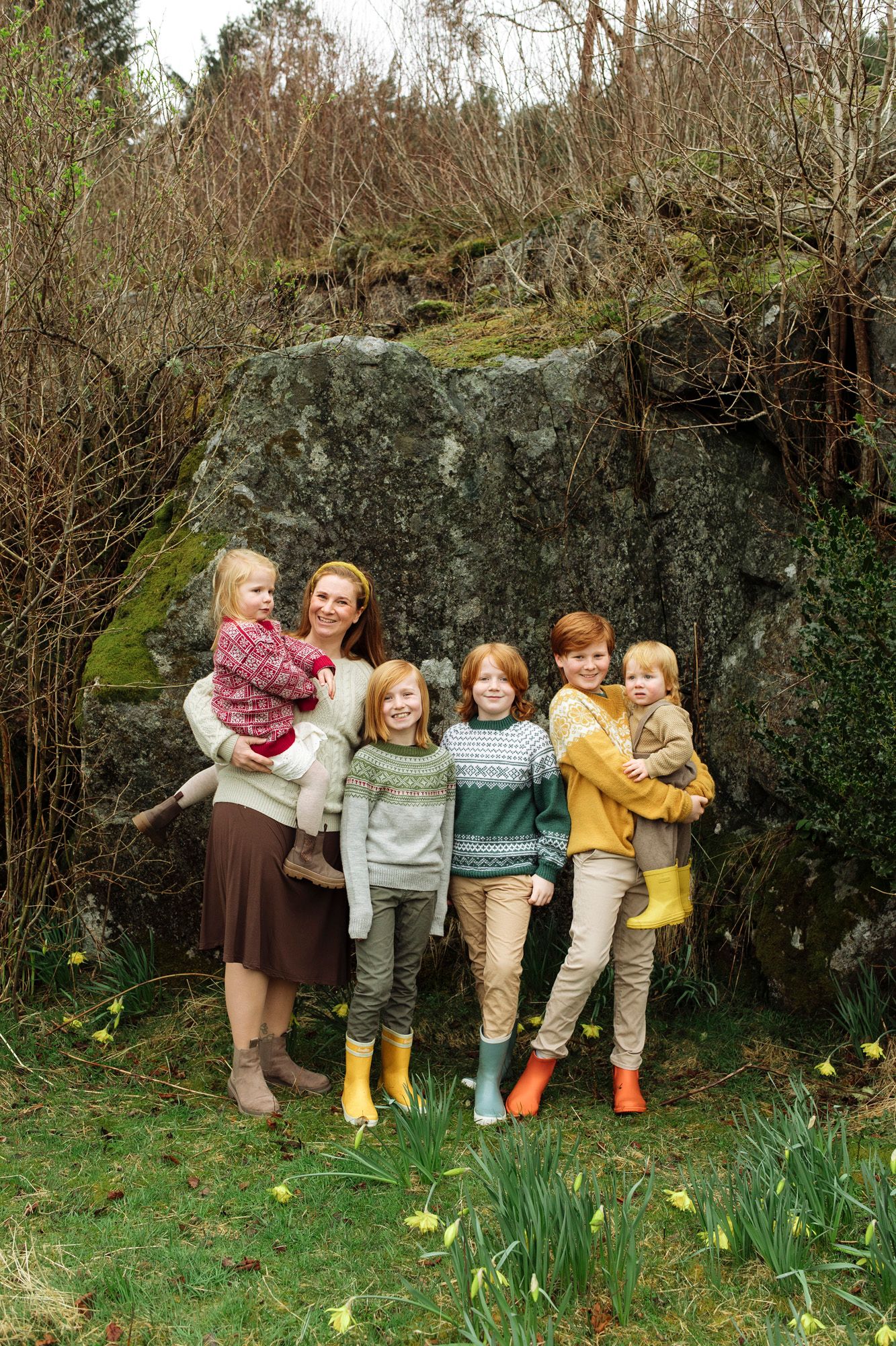 Group portrait against large mossy rock with coordinating sweaters and bright rubber boots.
