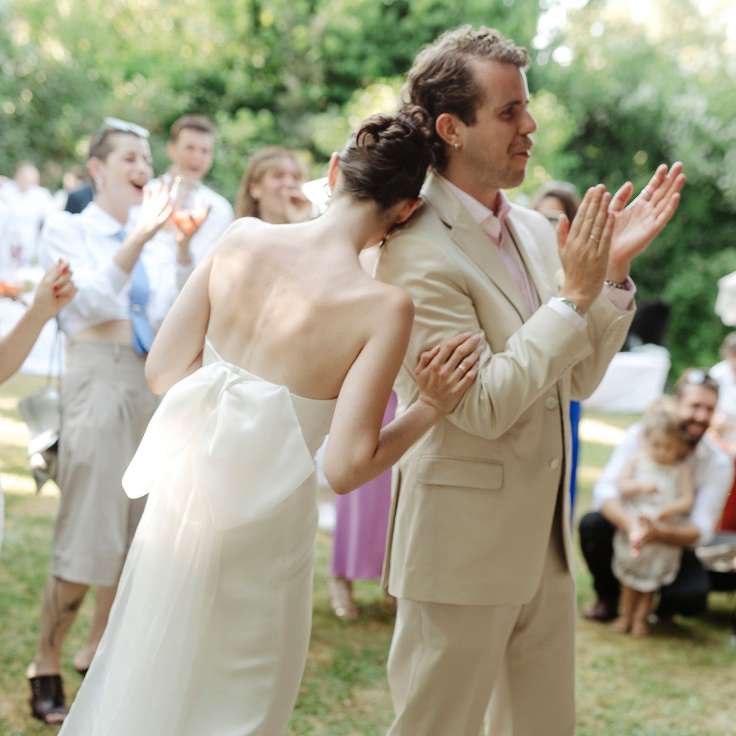 Wedding couple and guests dance joyfully in an outdoor garden reception setting.