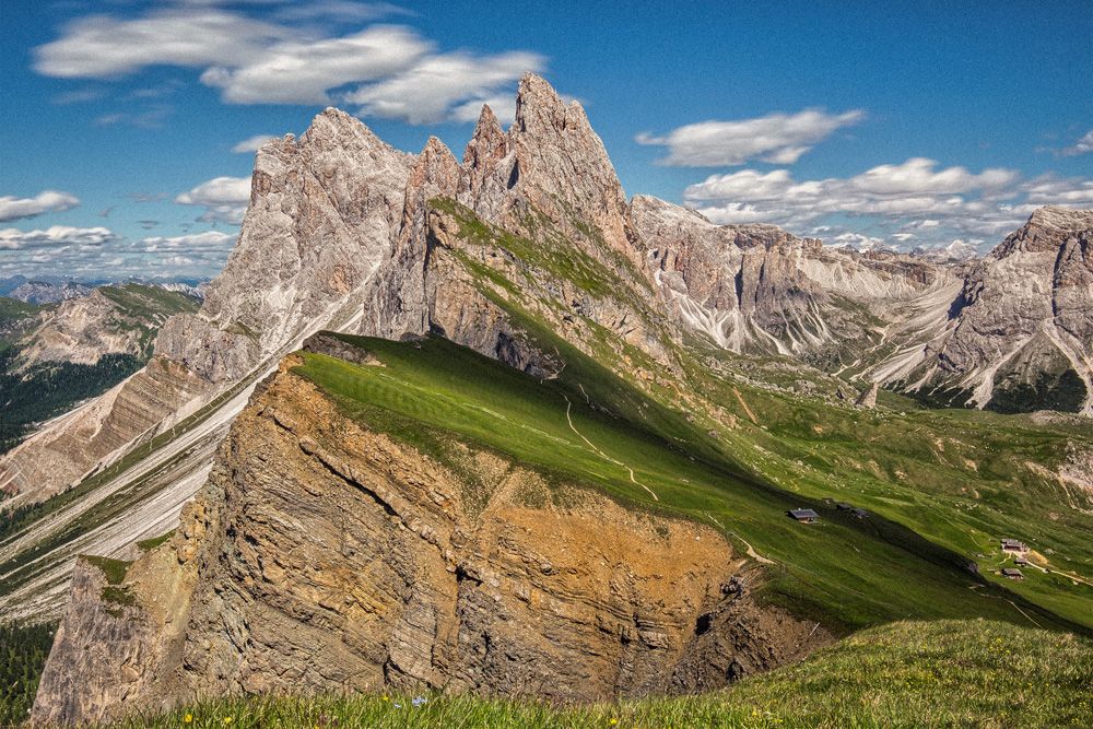 Panoramic vista of jagged mountain peaks and winding valleys under bright blue skies in the Dolomites.