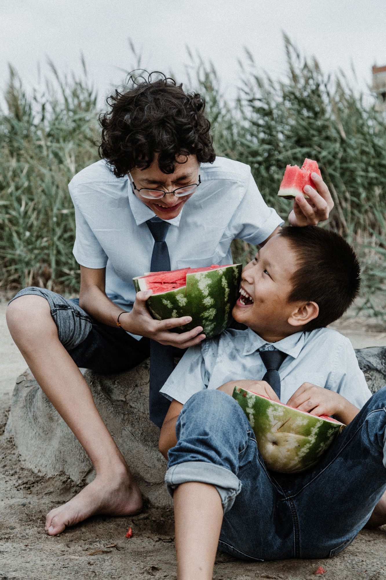 Two friends share a watermelon while sitting on the ground on a sunny summer day.