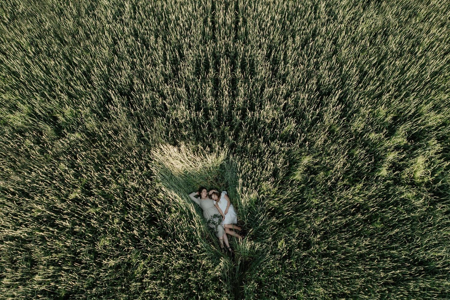 Two people lying in tall green grass field seen from above in a creative perspective shot.