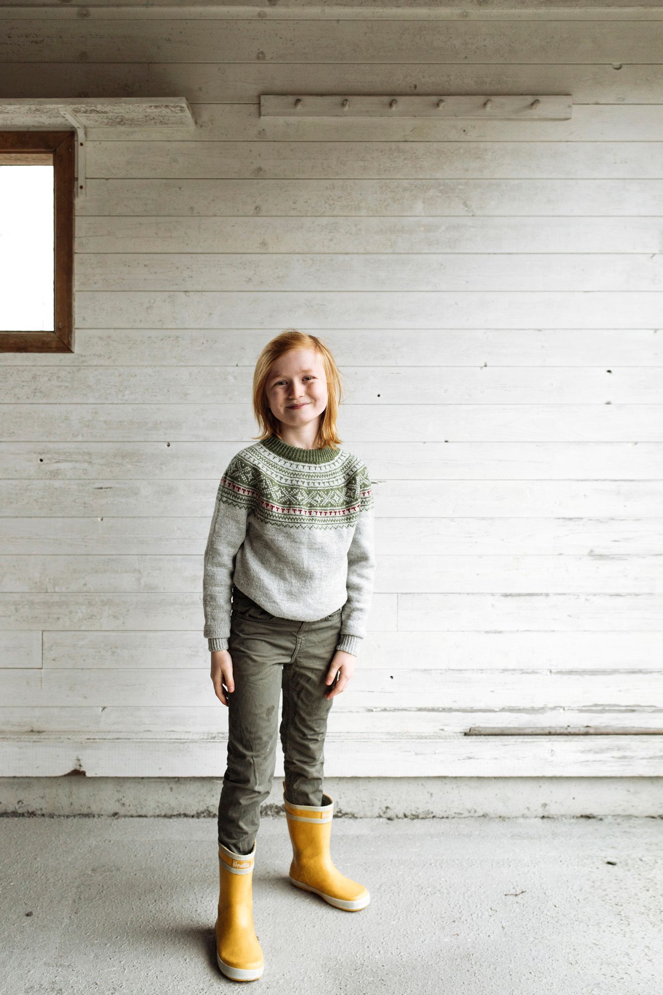 Stylish winter outfit featuring a patterned sweater and bright yellow rain boots in a minimalist white space.