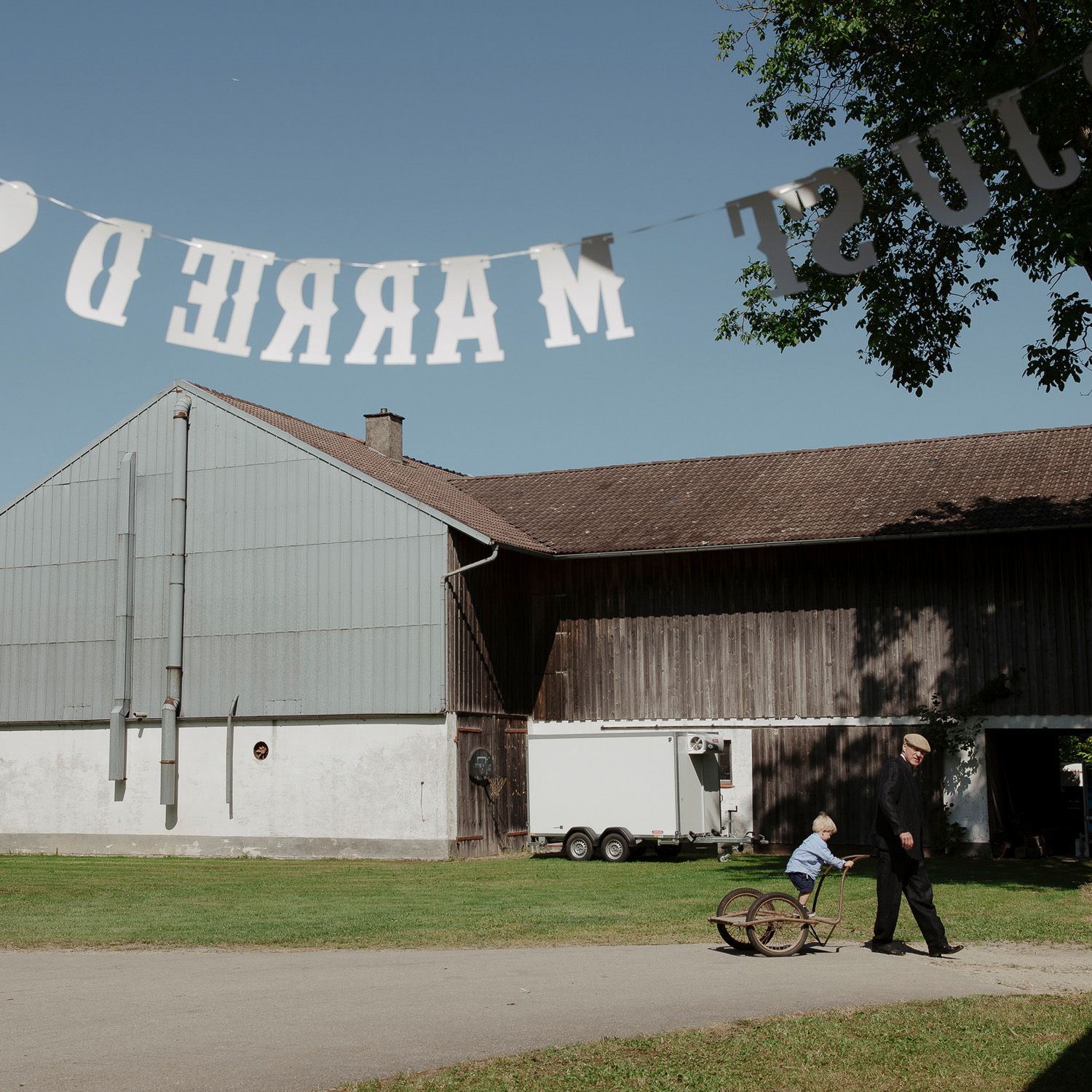 A series of white barns and farm buildings connected in a row against a blue sky and green grass.
