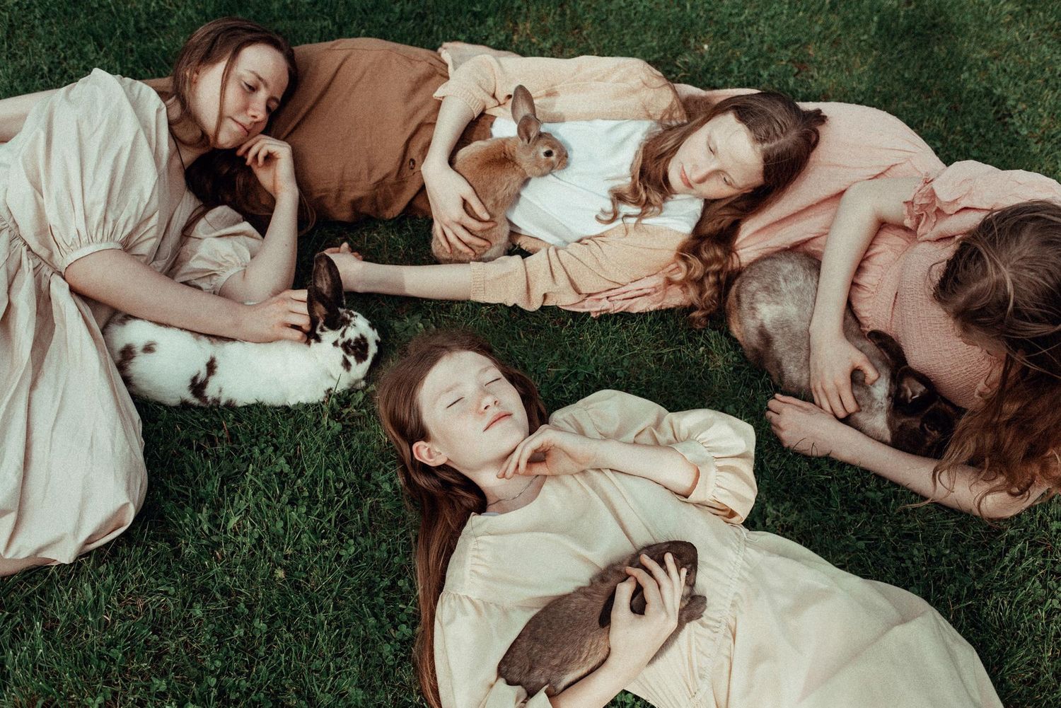 A group of people lying down on grass in white clothing creating an artistic circular formation.