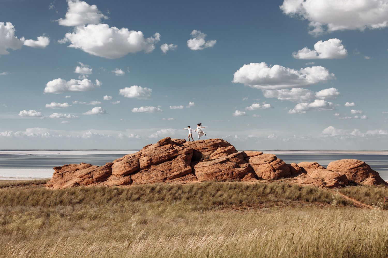 Panoramic view of coastal sand dunes and rocky outcrops under a bright blue sky with scattered white clouds.