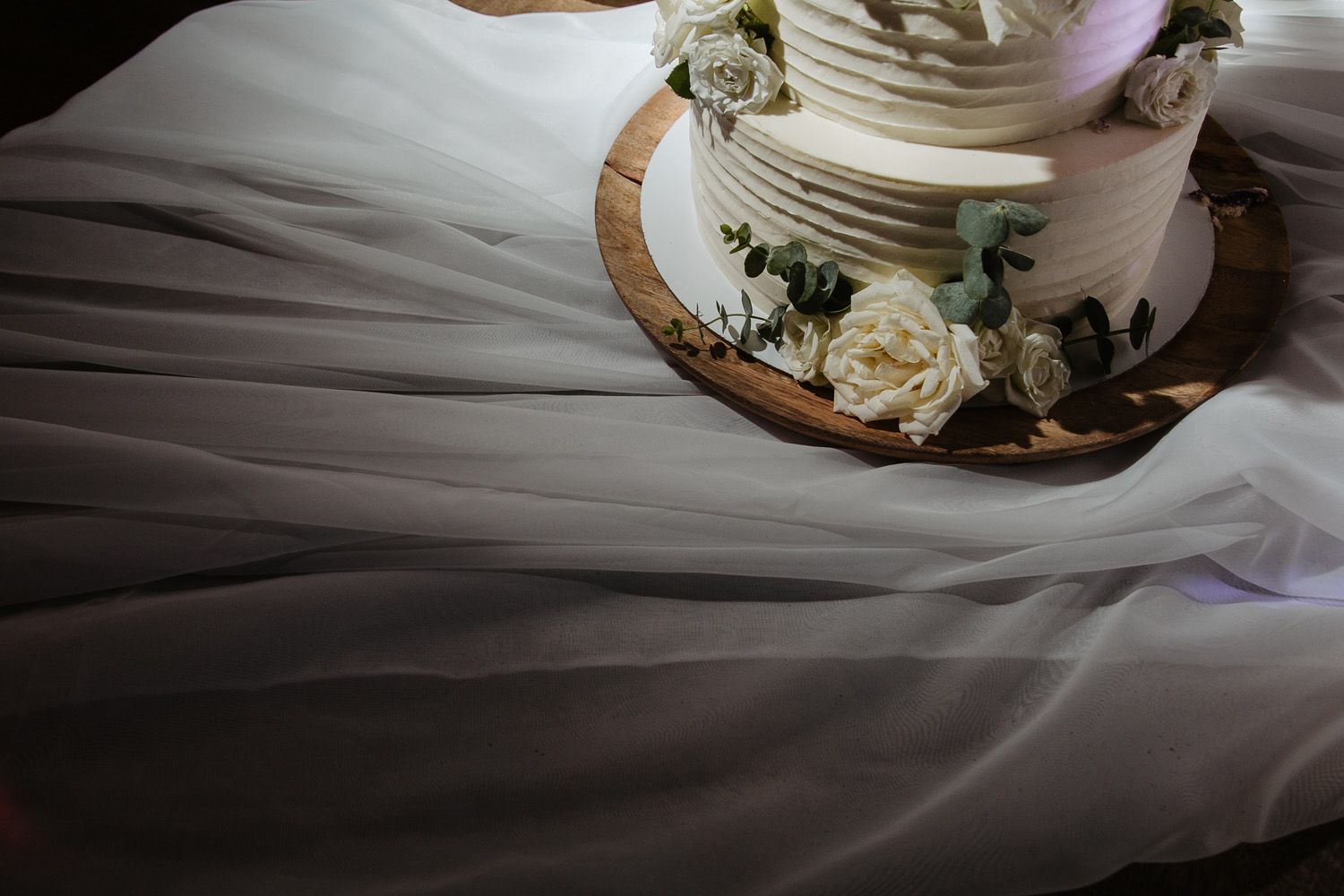 White wedding cake with floral decorations on a wooden table with elegant place settings.