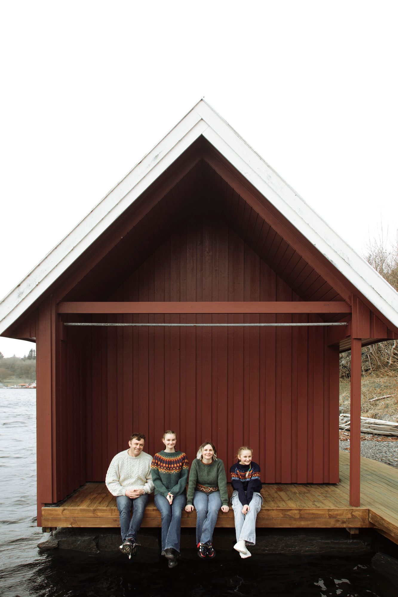Four wooden boat houses with brown siding sit along a waterfront dock as people rest on their steps.