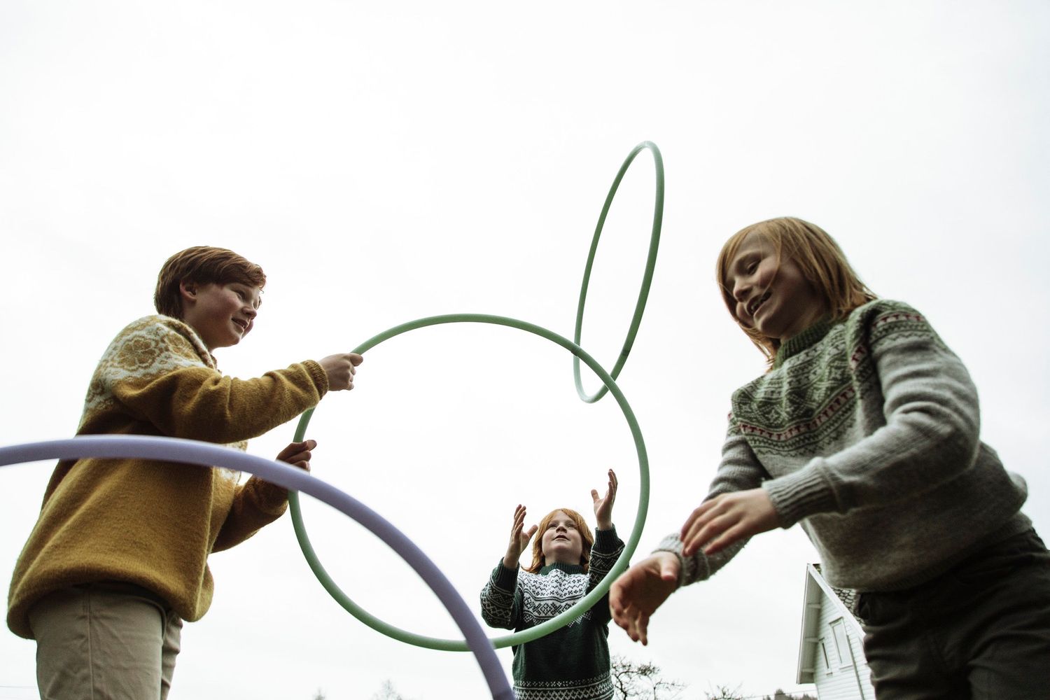 Three people playing with green and blue hula hoops against an overcast sky outdoors.