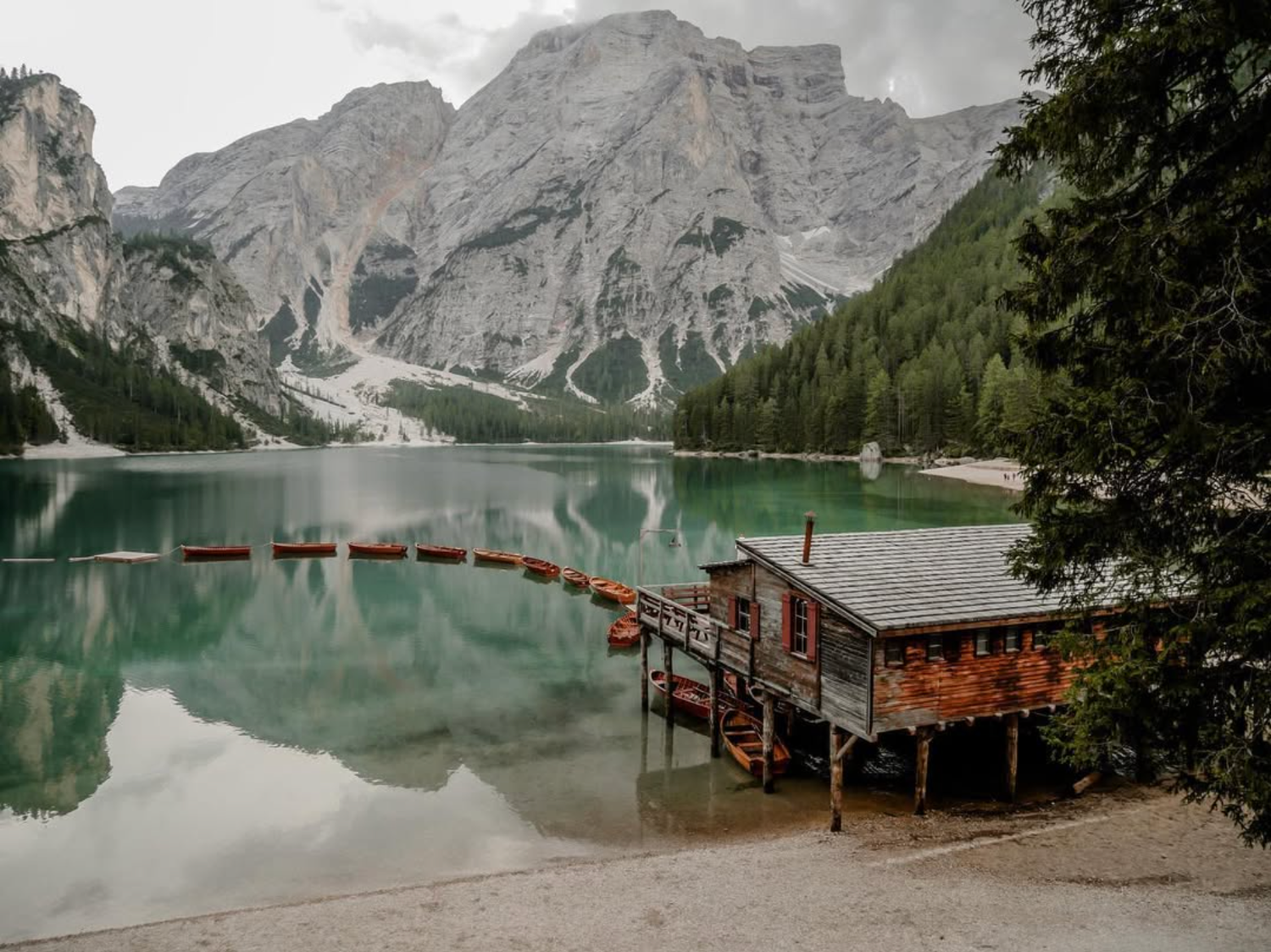 Wooden boardwalk along a pristine alpine lake surrounded by towering mountain peaks and dense forest.