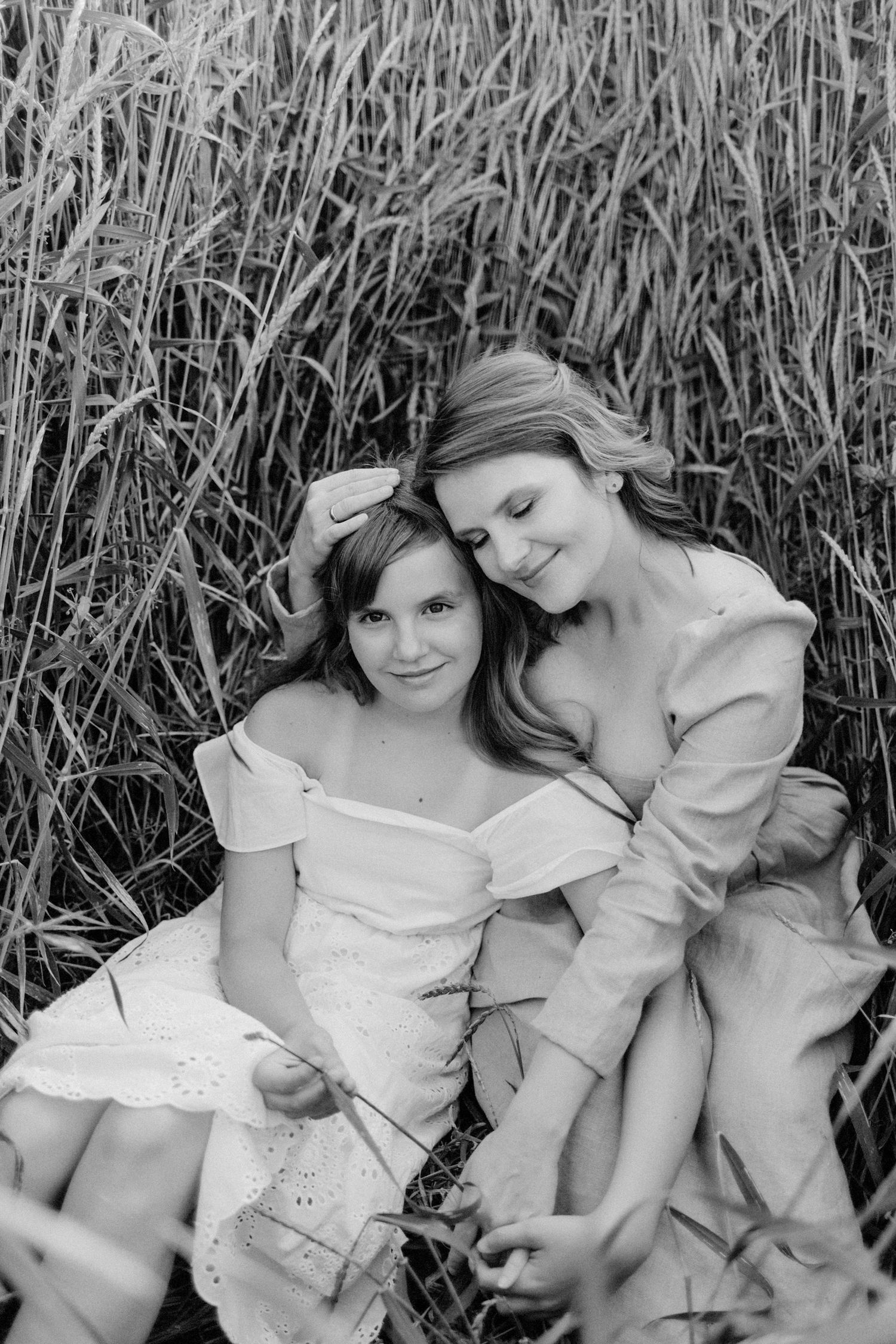 Two people in white dresses laying in a wheat field creating an artistic black and white composition.