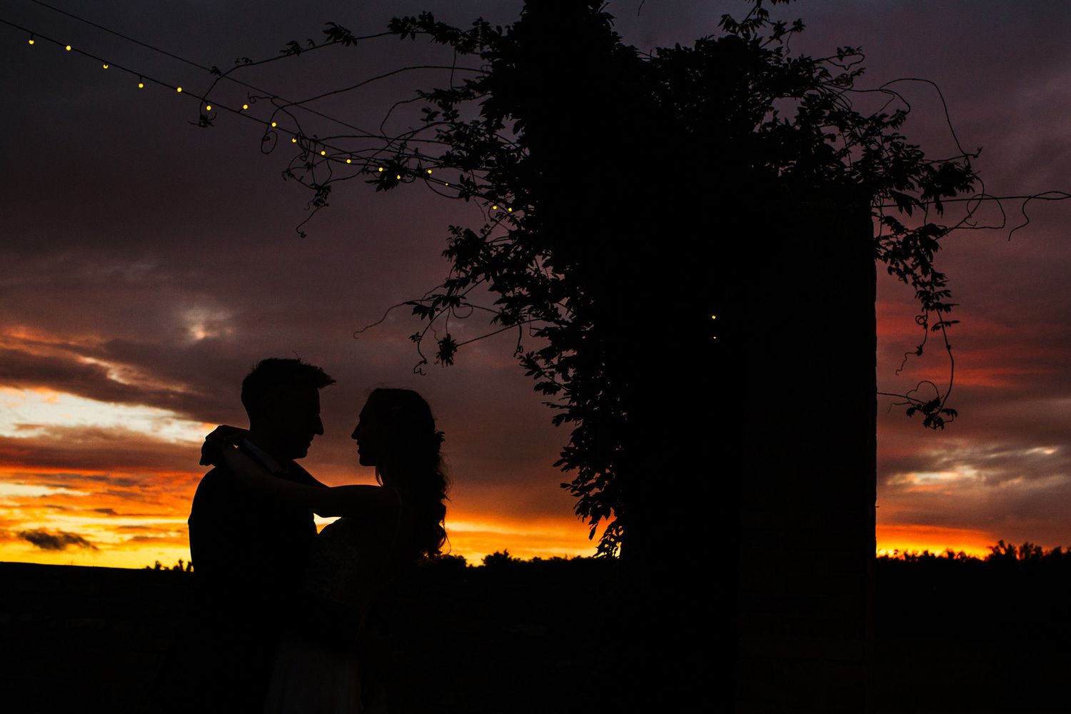 Two silhouettes embrace against a dramatic orange and purple sunset sky.