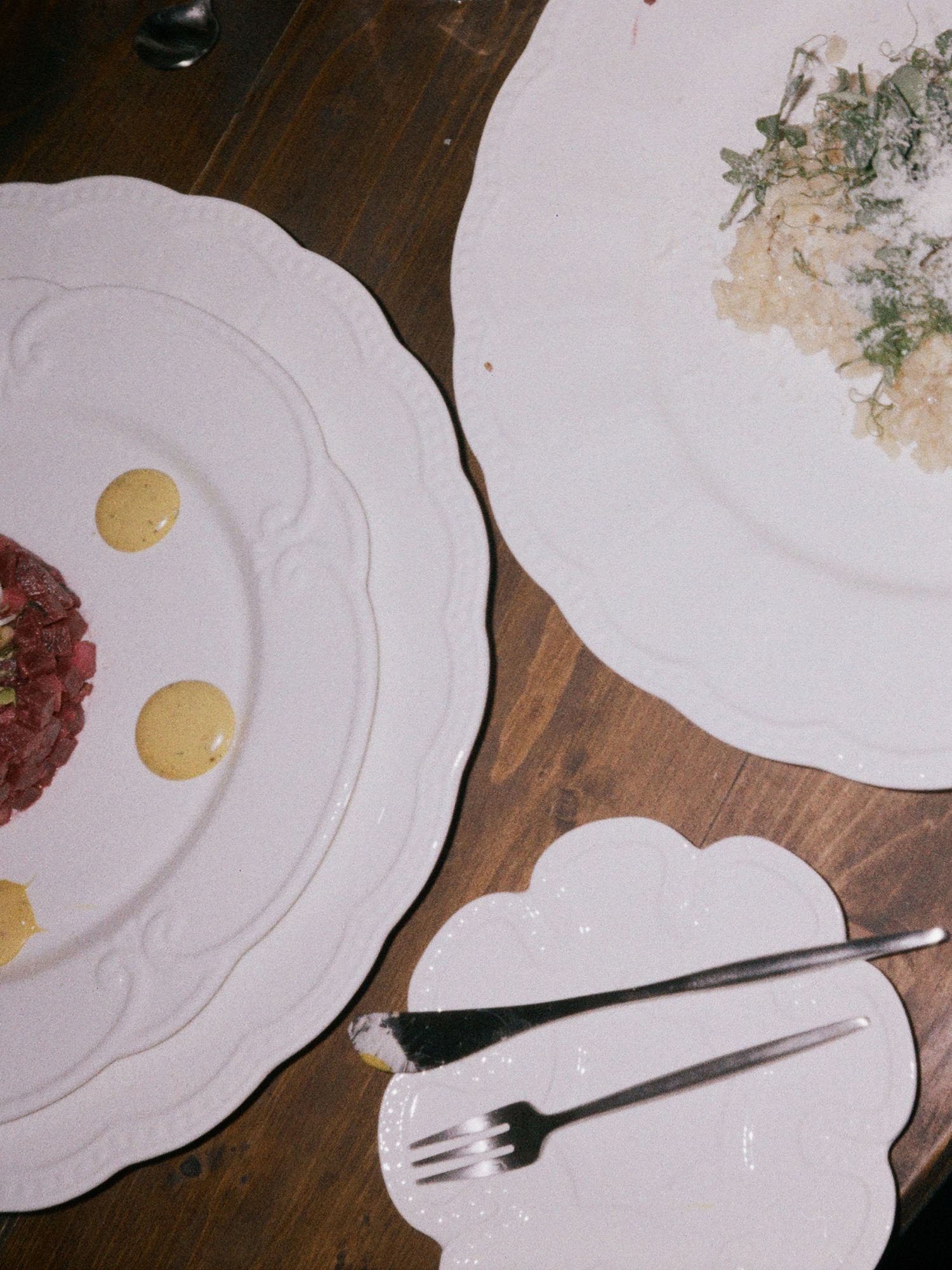 White plates with food remnants and sauce stains arranged in a row on a dark wooden surface.