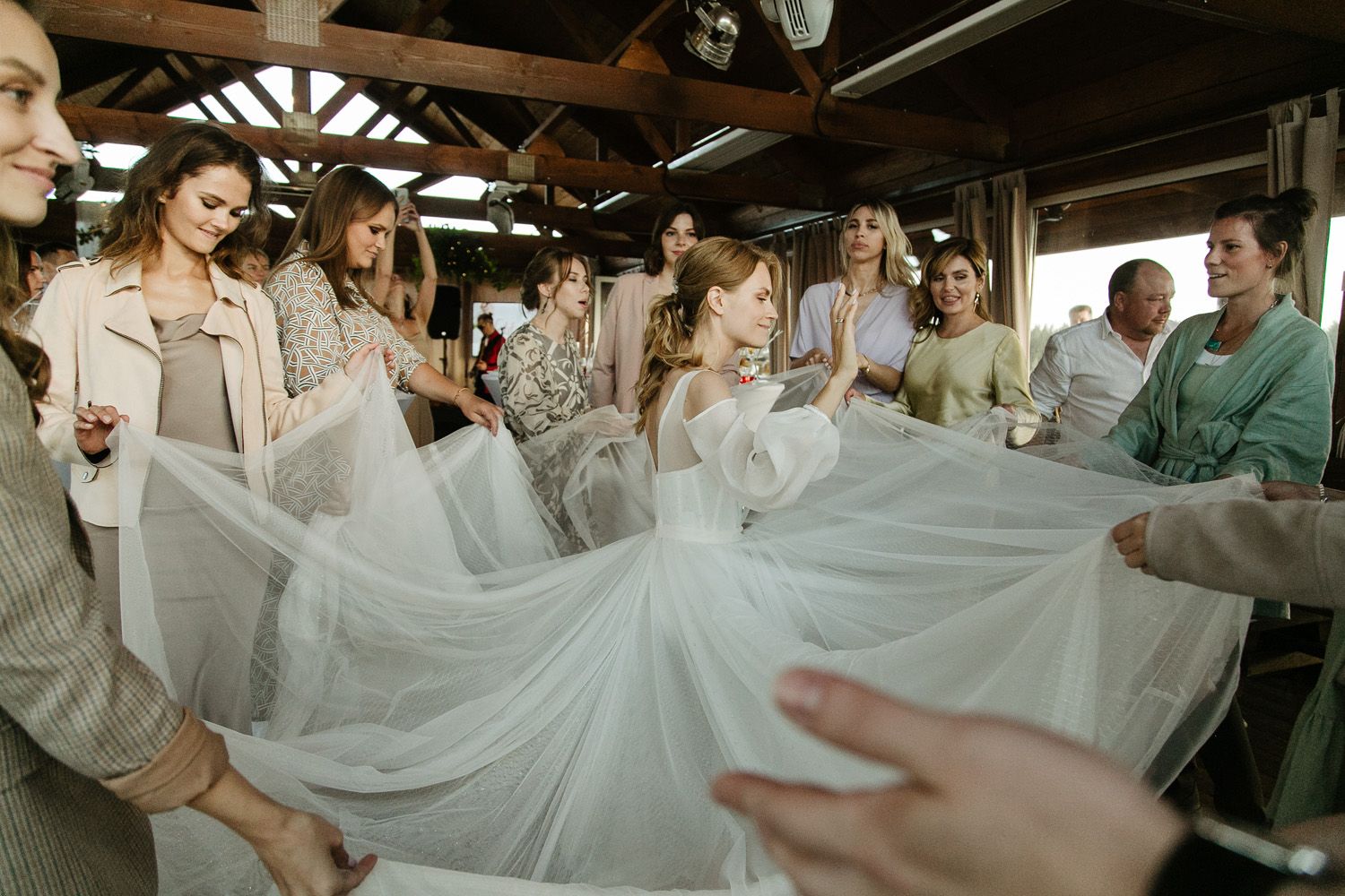 Wedding guests hold up a flowing white fabric in celebration during an indoor reception.