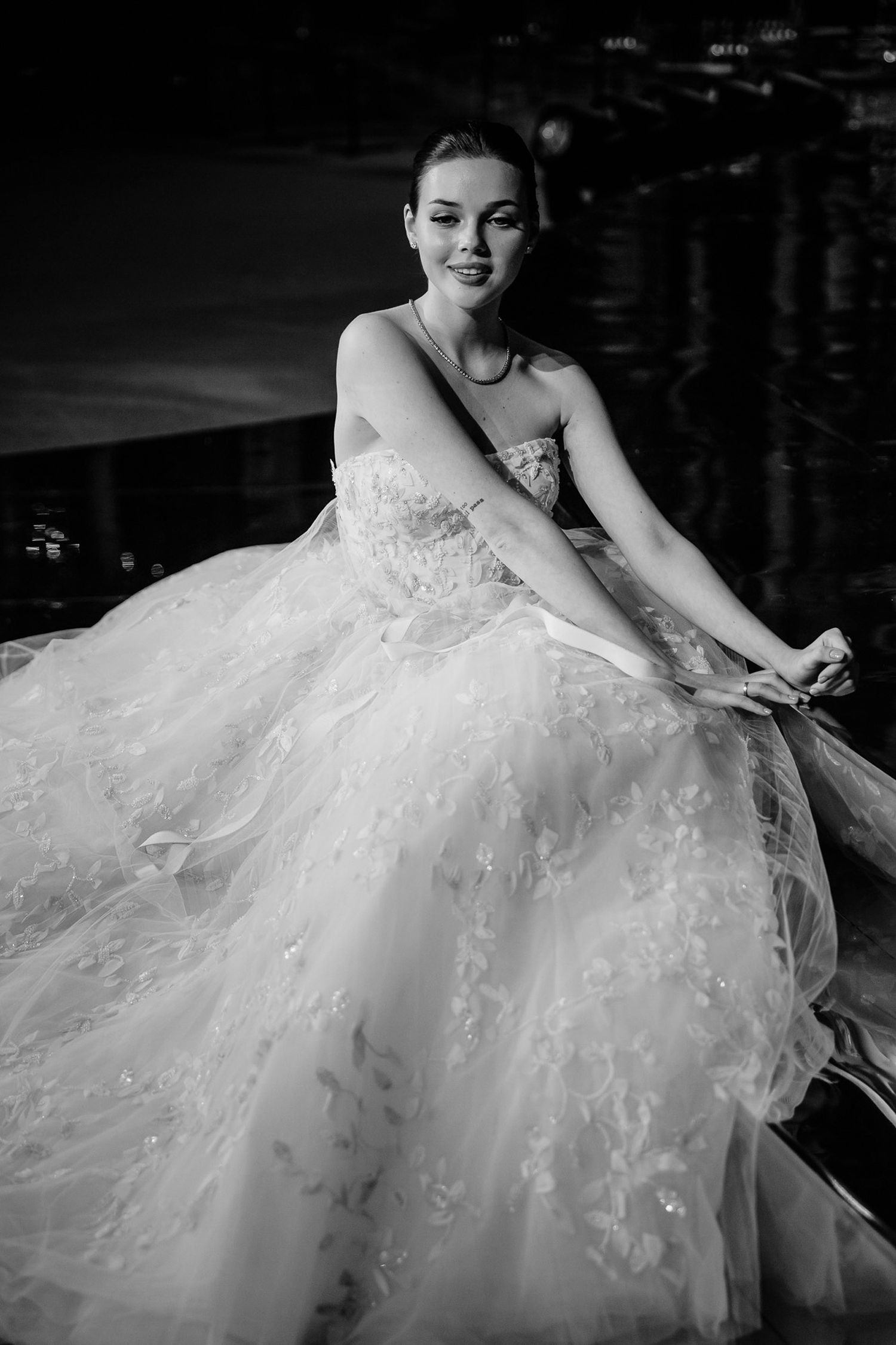 A bride in a luxurious white tulle gown with lace details poses elegantly in black and white photography.