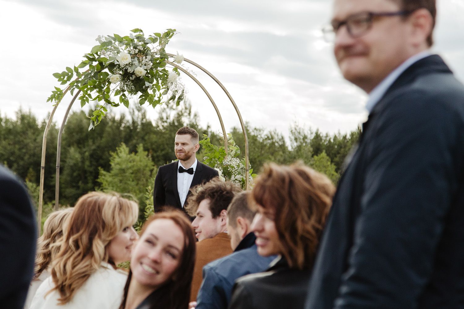 Wedding ceremony under floral arch with guests gathered outdoors.