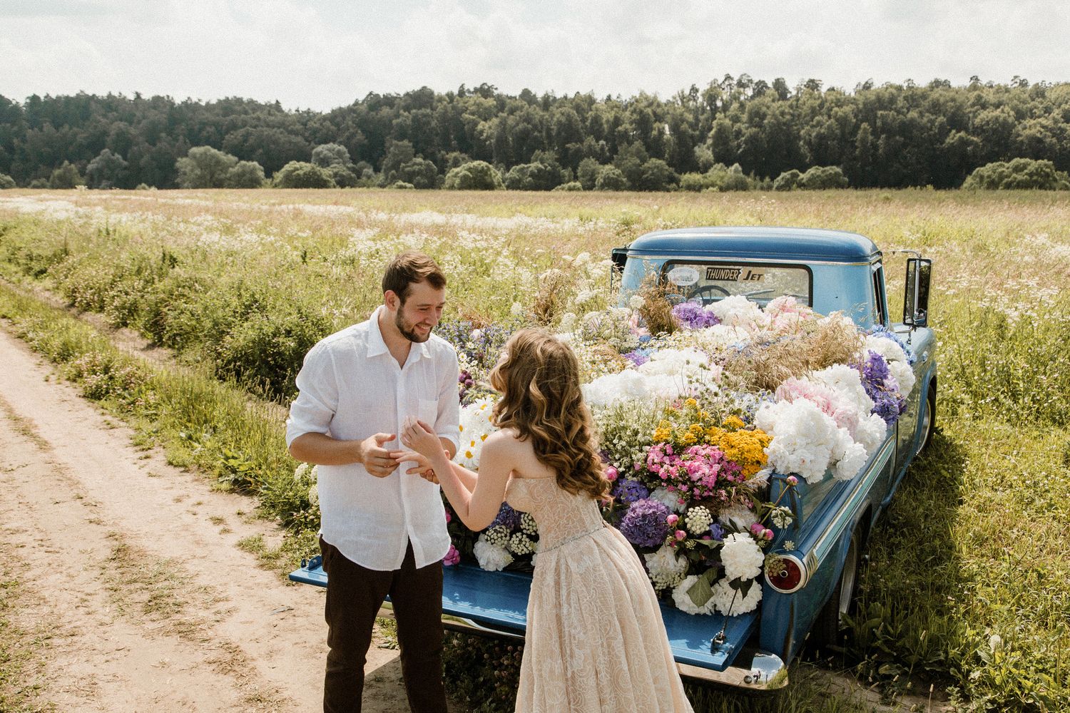 Vintage blue truck parked in a sunny meadow during a summer celebration with floral decorations.